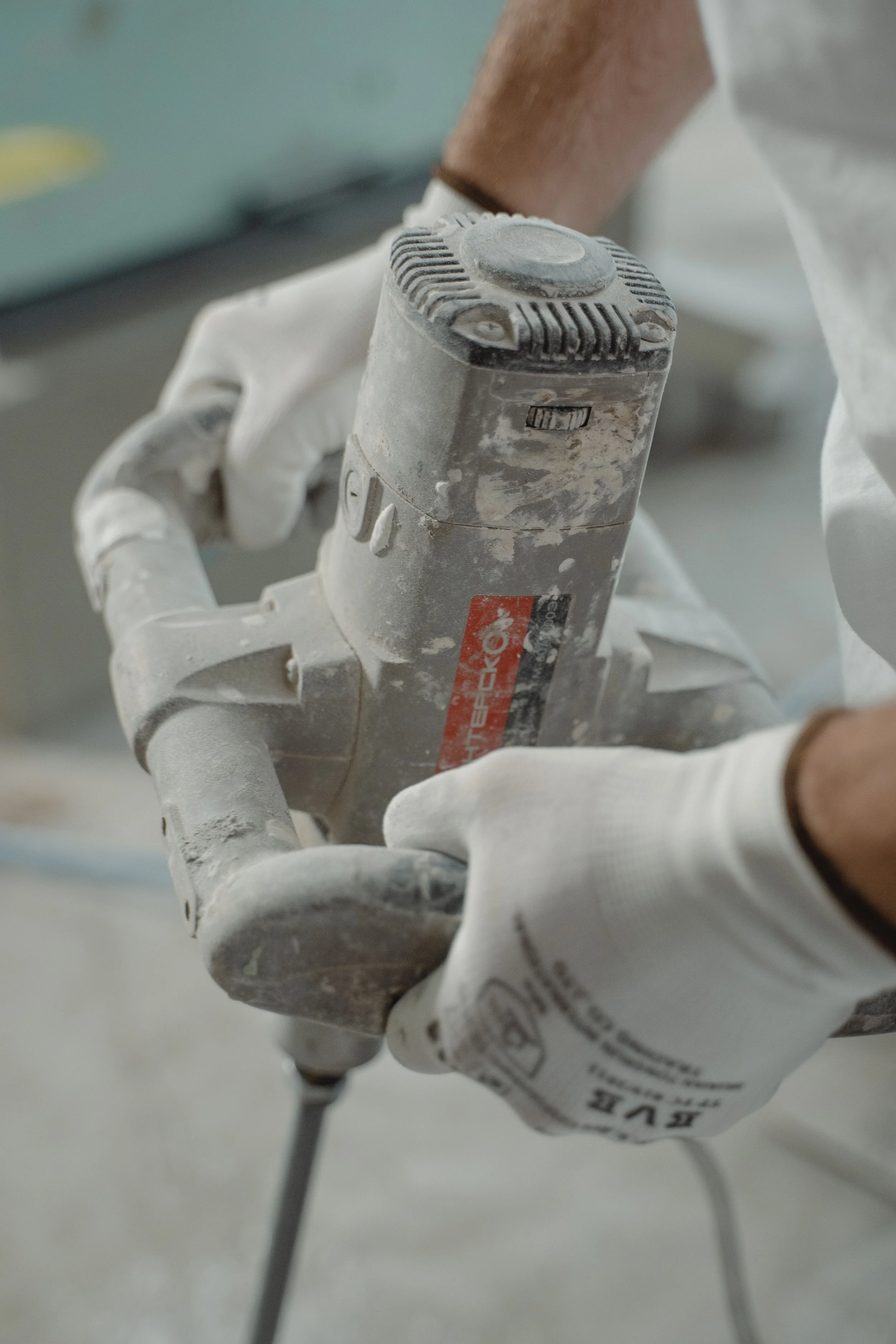 Close-up of a person wearing white gloves holding a dusty electric power drill.