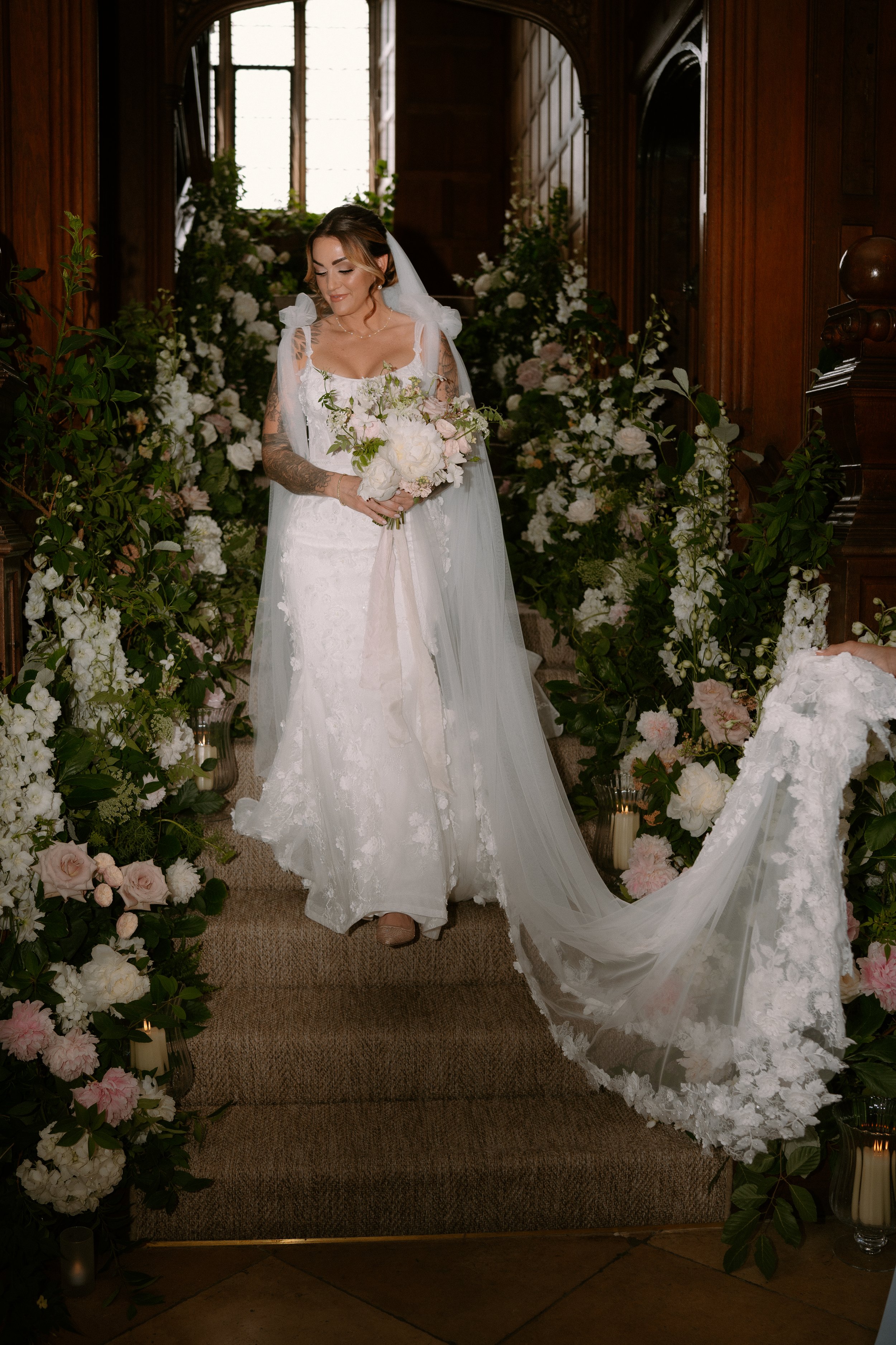 Bride in a white wedding gown holding a bouquet stands in front of a floral arch inside a wood-paneled church.