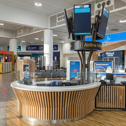 Airport information kiosk with multiple screens and a curved wooden counter.