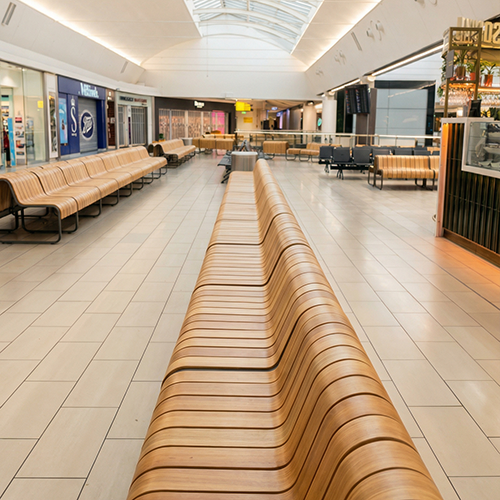 Empty airport terminal with rows of brown seats and a large digital screen in the background.