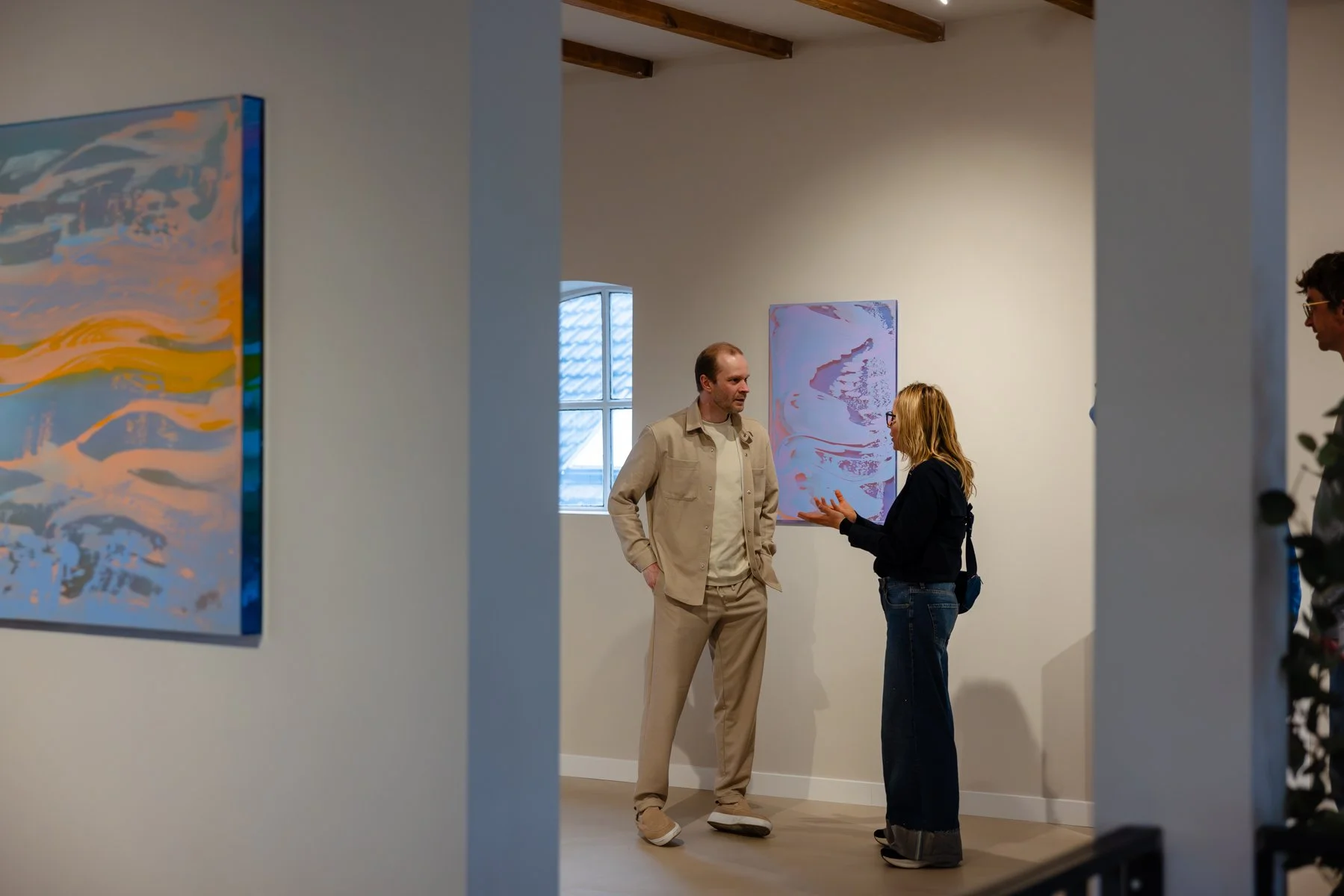 Visitors talking at the gallery, surrounded by abstract paintings by Lisette Schumacher
