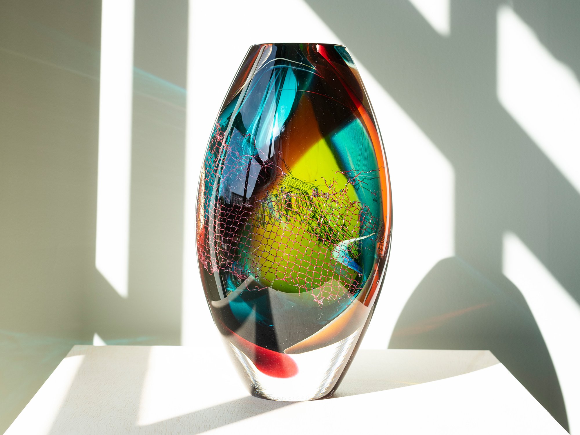 Contemporary glass sculpture by Francisca Snel showing copper mesh through turquoise and amber glass