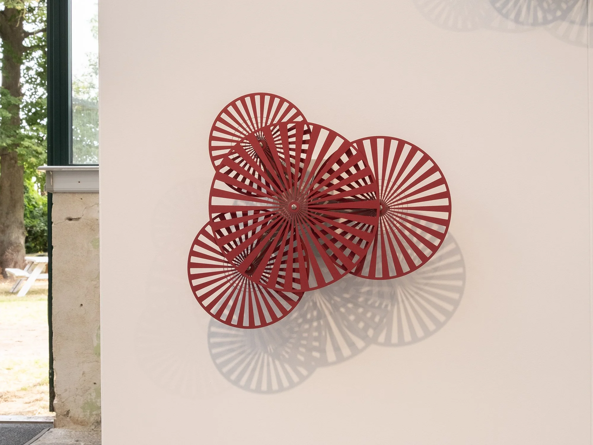 Wall-mounted kinetic sculpture in red anodised aluminium by Freerk Wilbers, activated through touch and designed around rhythm and movement.