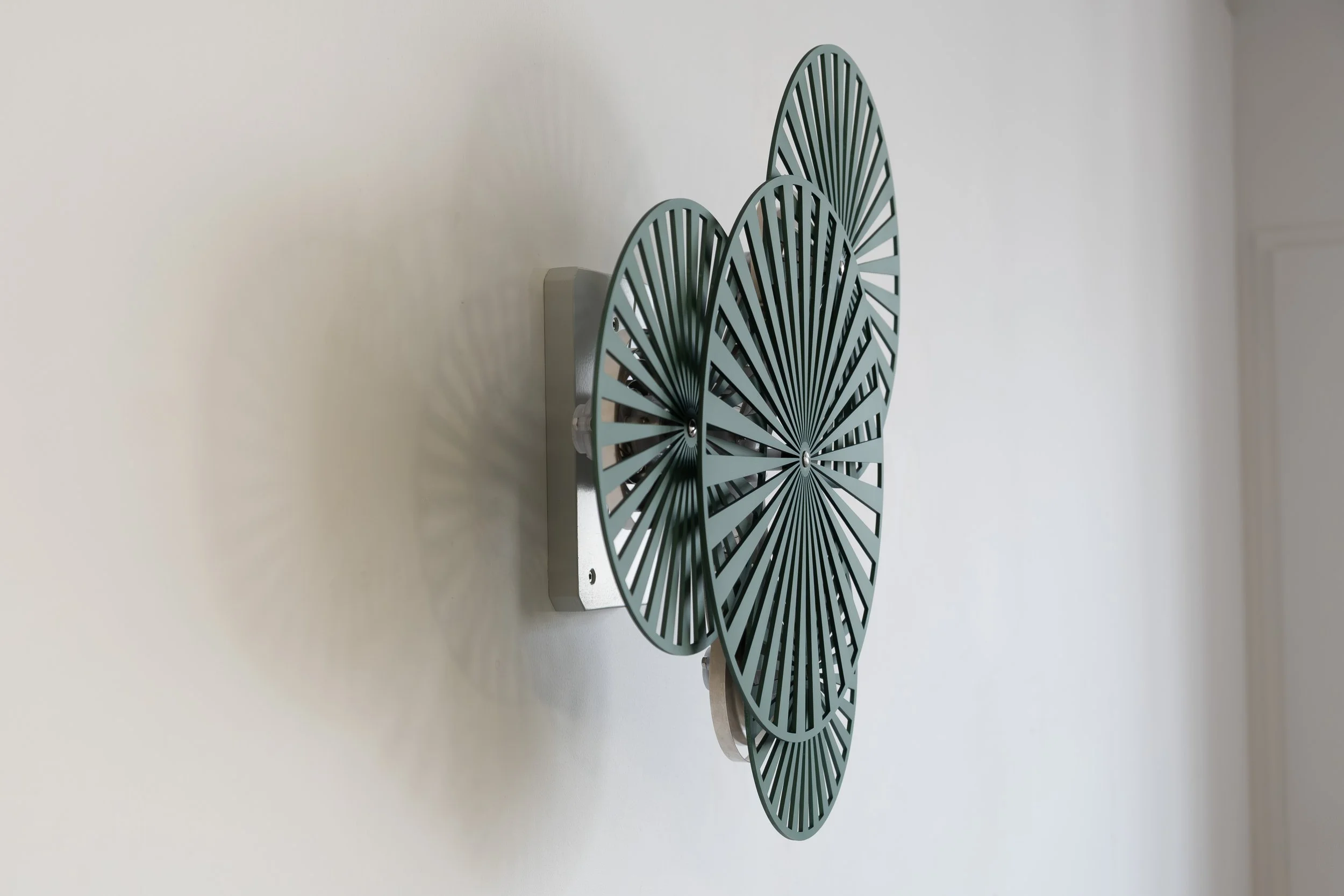Wall-mounted kinetic sculpture by Freerk Wilbers in green anodised aluminium, exploring rhythm and chance through movement.