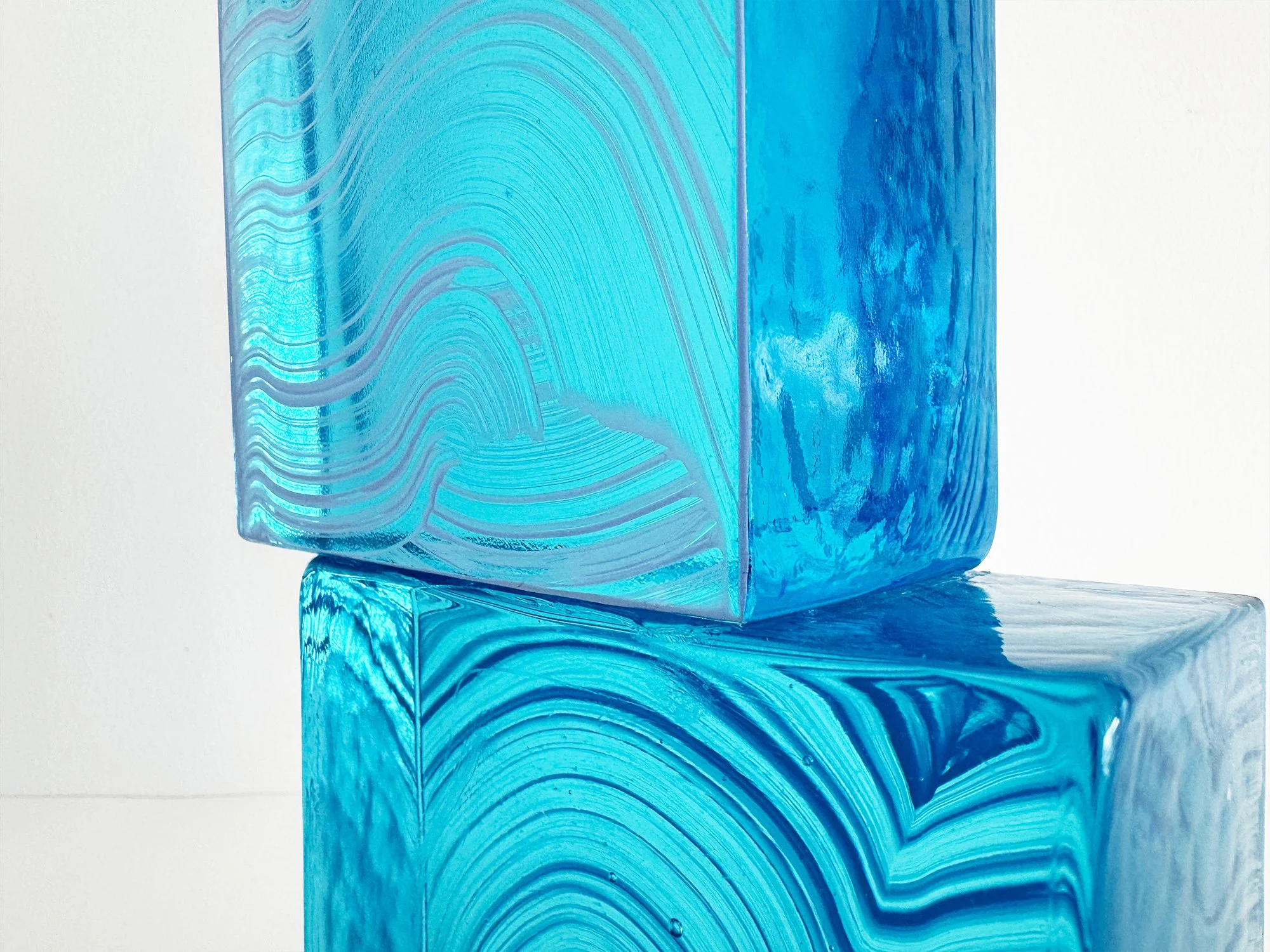 Detail of cast glass sculpture showing flowing layered lines and internal depth in turquoise and blue glass
