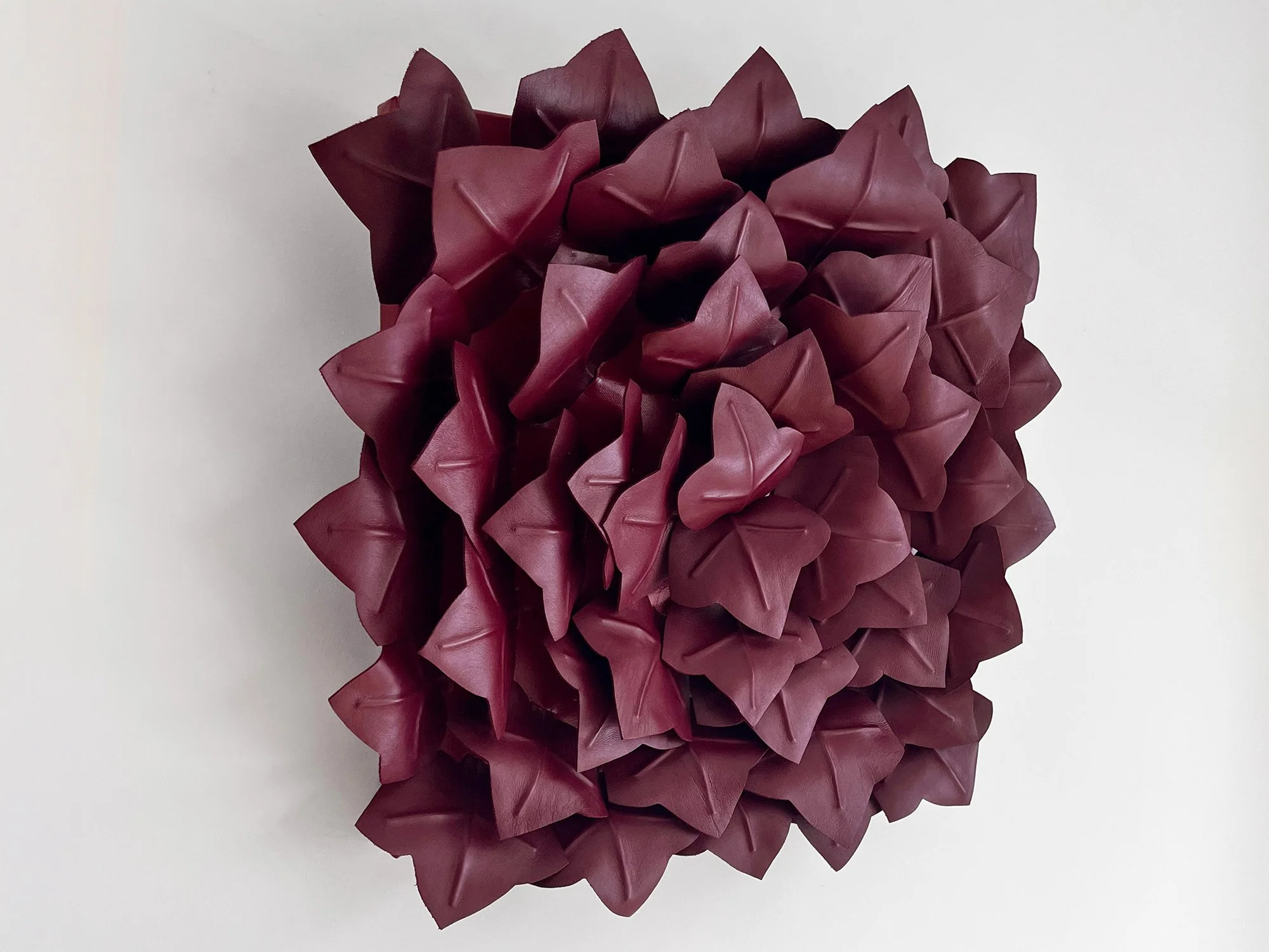 Contemporary leather artwork with layered geometric folds in deep red tones