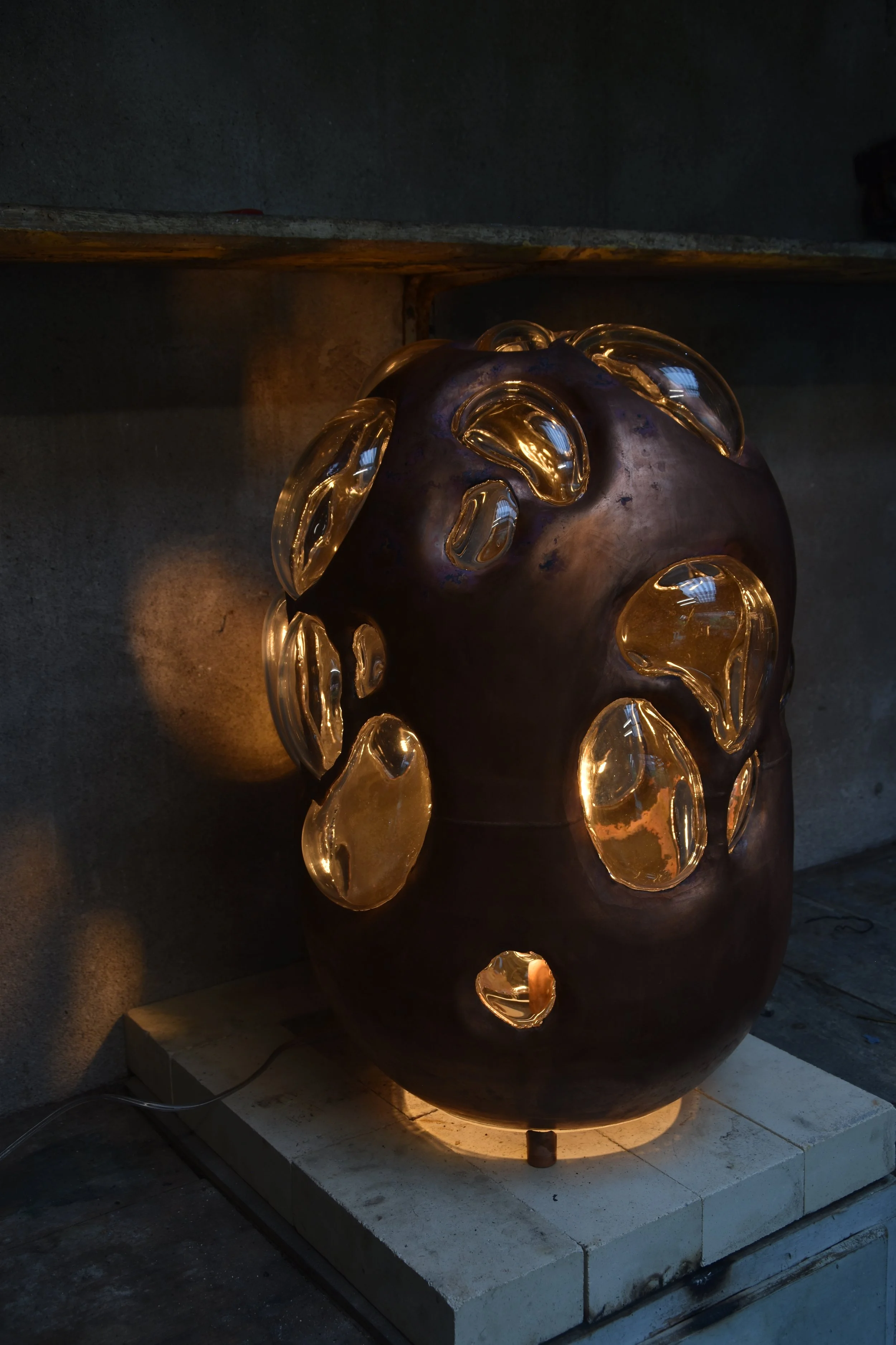 Copper and glass light sculpture by Anna Oudhof photographed in the workshop while illuminated.