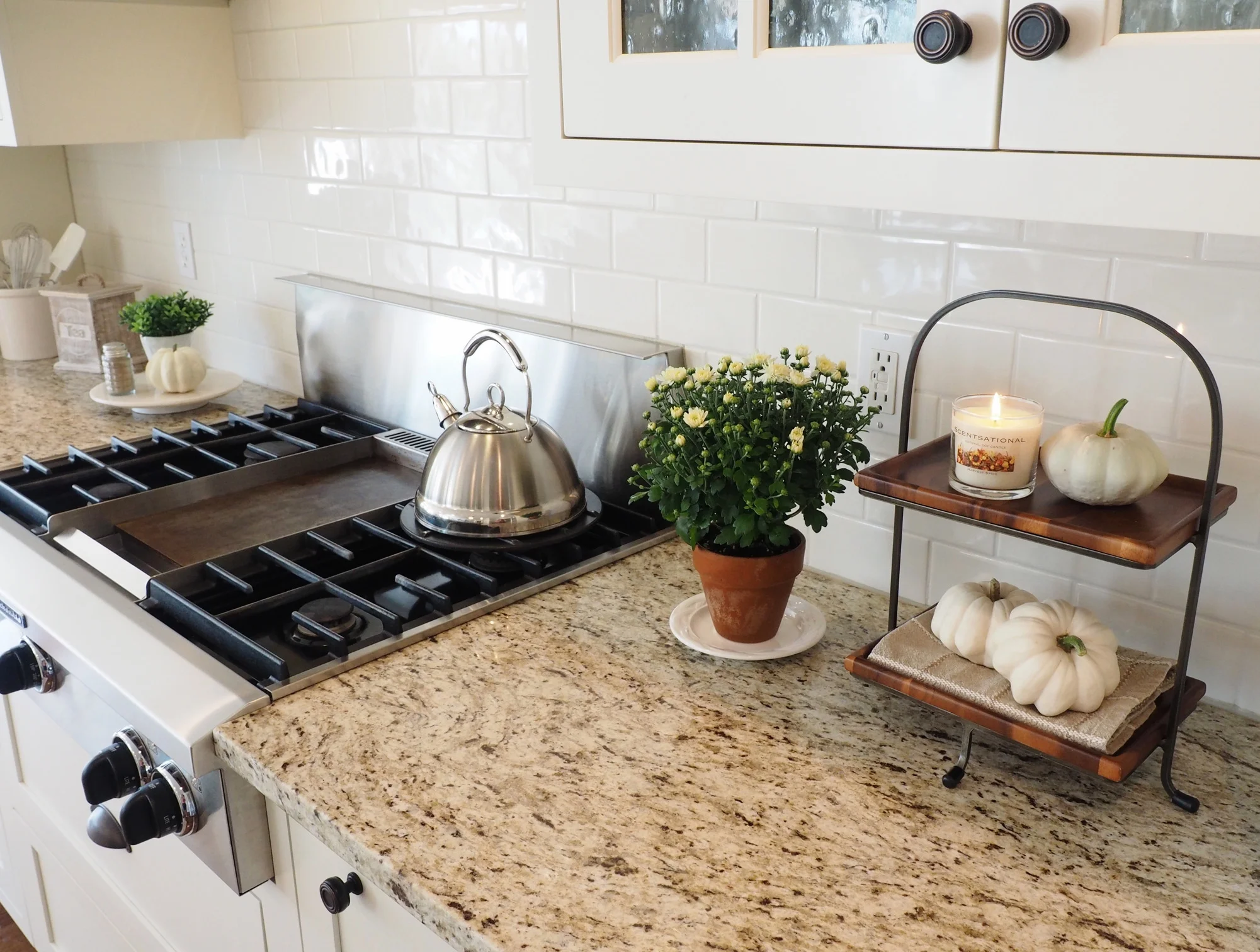 I like to add wood and iron details to my kitchen decor for the fall. It has an earthy feel and goes very well with our granite countertops. The granite is Giallo Ornamental. It's a very neutral granite and looks great with white or off-white cabinetry. It has a creamy background and touches of gray, taupe and dark brown. It truly is one of my favorite granite choices and I believe readily available and within an affordable price range. Our gas cooktop is made by Kitchen-Aid featuring the center griddle. I have fried hamburgers, made pancakes and grilled cheese sandwiches on our griddle with ease however, since our children are gown now, my use for it has declined. Today I would opt for the 6 burners. But hey, you never know what life will bring your way when making these choices.