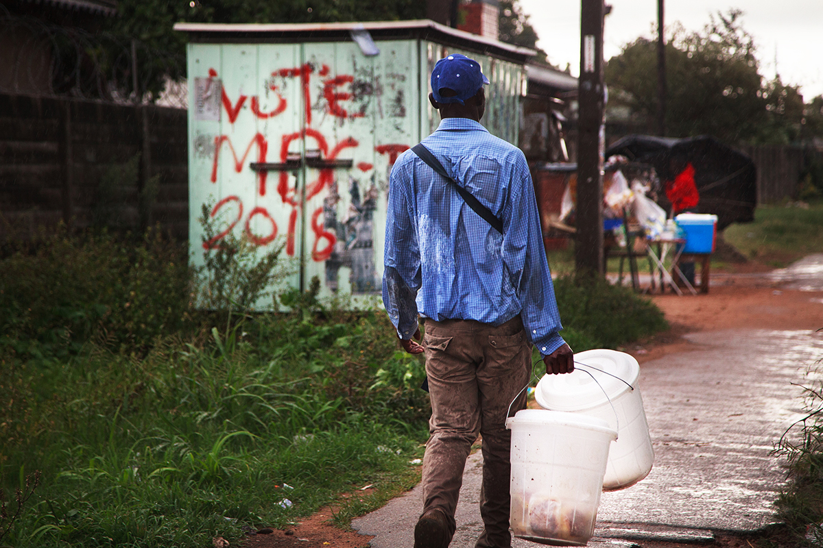 January 1, 2018: A man selling homemade doughnuts walks past graffiti sprayed onto an electricity sub-station on a rainy day in Engineering, Highfield, Harare. The surburb, which is the second oldest in Harare, was home to former President Robert Mugabe in the 1960s and is the birthplace of ZANU PF. - For Deutsche Welle