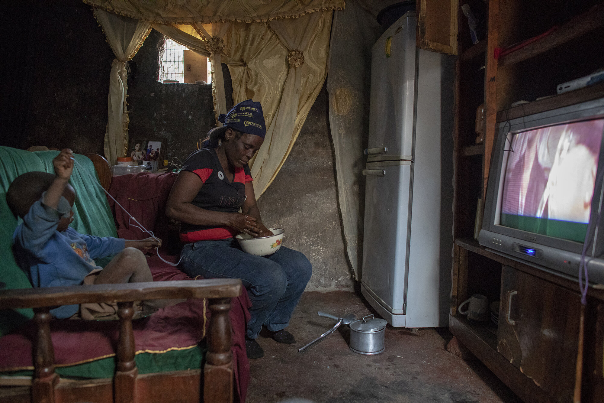  October 21, 2018: Roselyn washes he hands after having dinner at home while watching TV with her son Brendon in their one-roomed house on the farm compound.  
