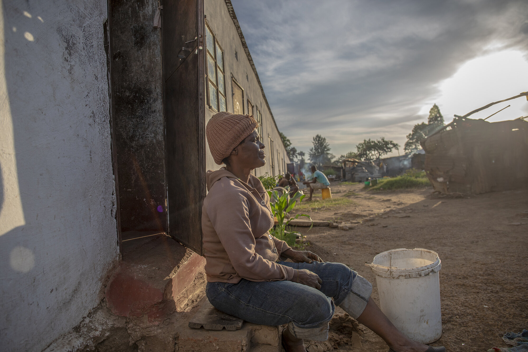  October 22, 2018: Roselyn takes a moment to rest at her doorstep after work in the farm compound. She is a single mother of 4 who lives in a one-roomed house. Growing up she was a Jehovah’s Witness and wanted to work at the church offices and at som
