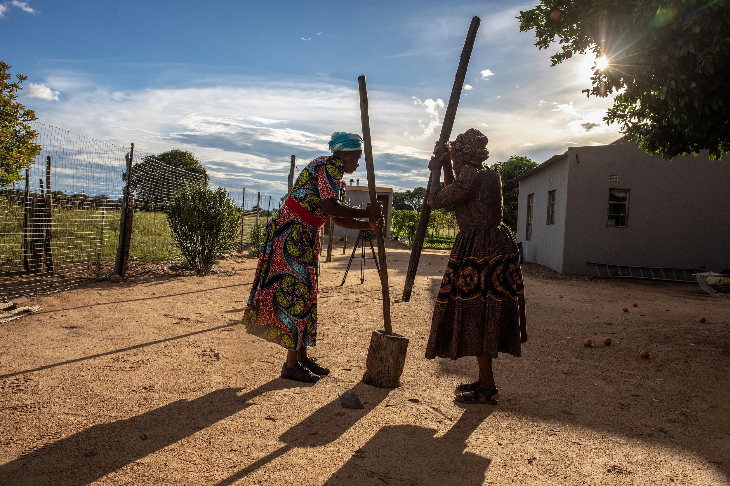  Vina Lundi and Sobuhle Phiri work together to pound millet in a large mortar. -  For Help Germany  