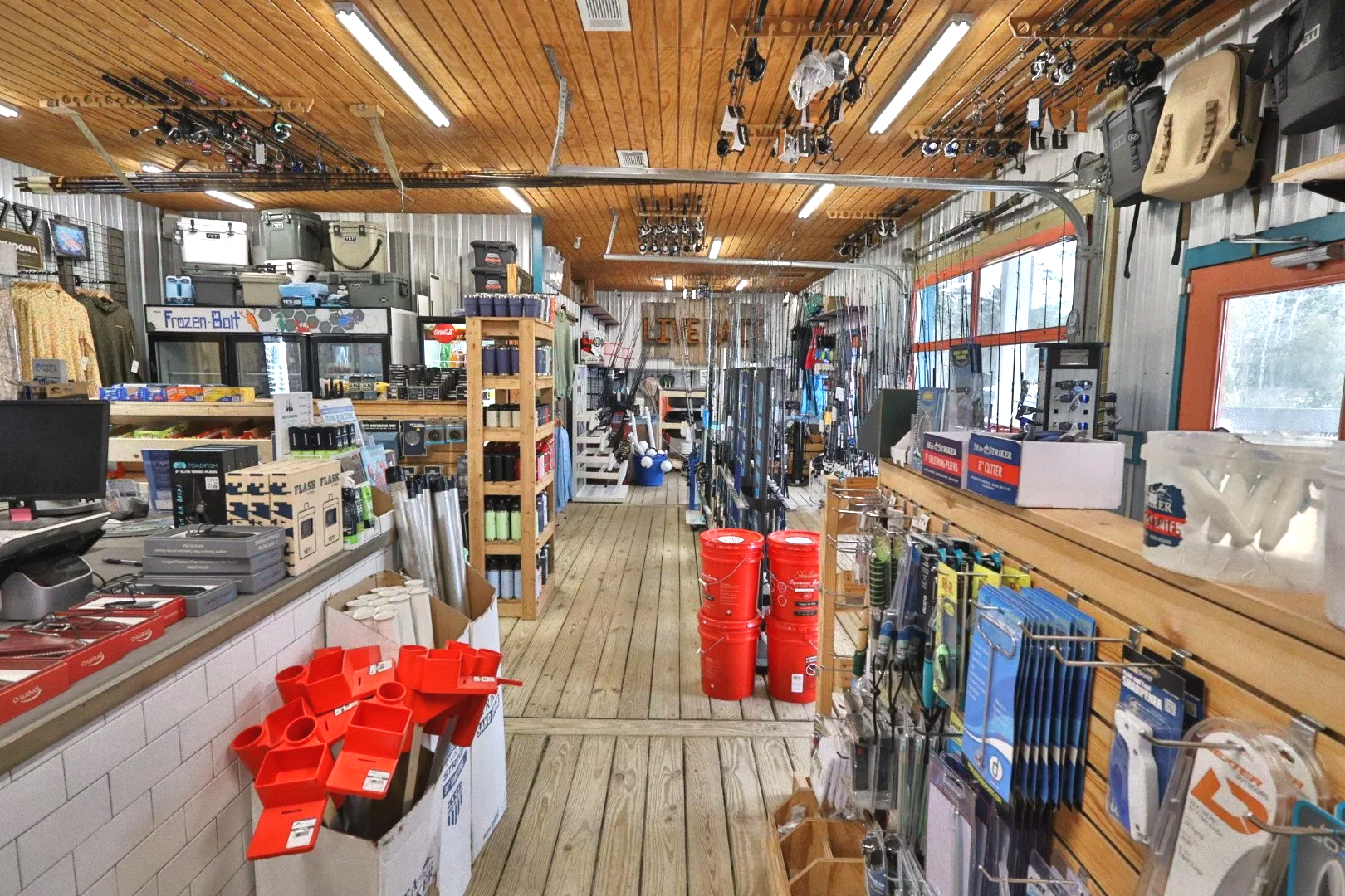 Interior of a sporting goods store with fishing and outdoor equipment, including rods, reels, fishing supplies, and buckets.