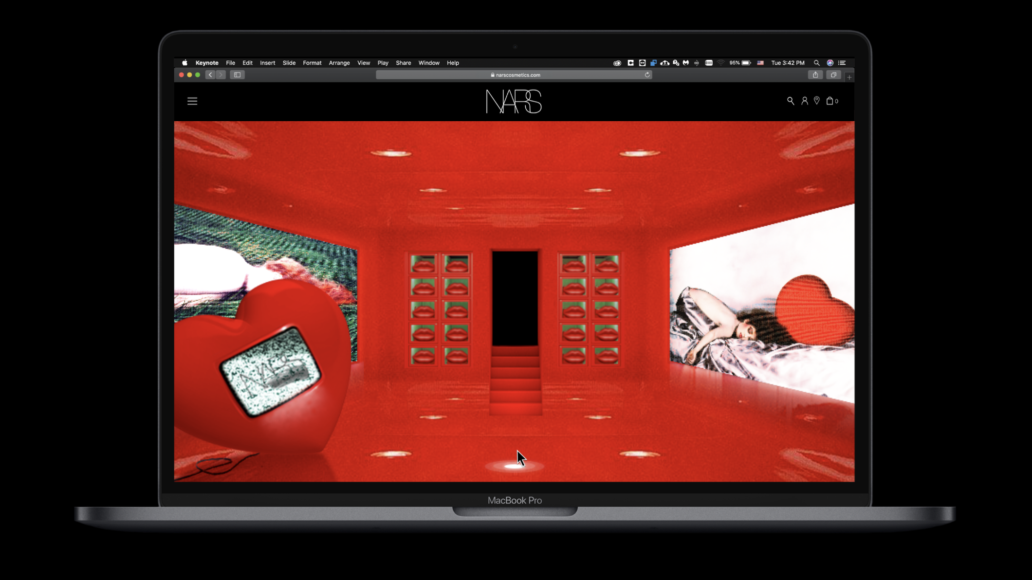 Laptop screen displaying a red-themed digital art exhibit with bottomless stairs, a large red heart-shaped sculpture with a screen, and a woman lying on a bed with a large heart-shaped pillow.