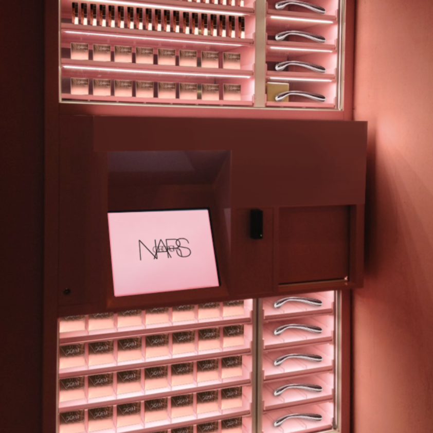 Display case with various lipsticks and makeup products, with a digital screen showing the NARS logo in a retail store.