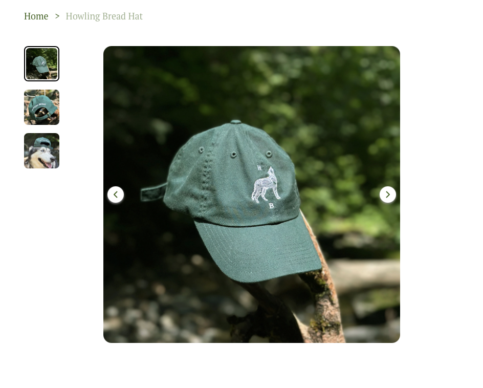 Green baseball cap with white embroidered dog and initials, placed on a tree branch outdoors with blurred green foliage background.