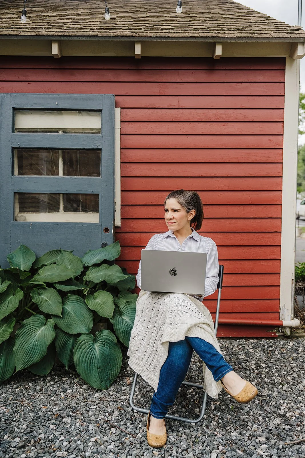 A woman sitting outdoors typing on a laptop outside a red building