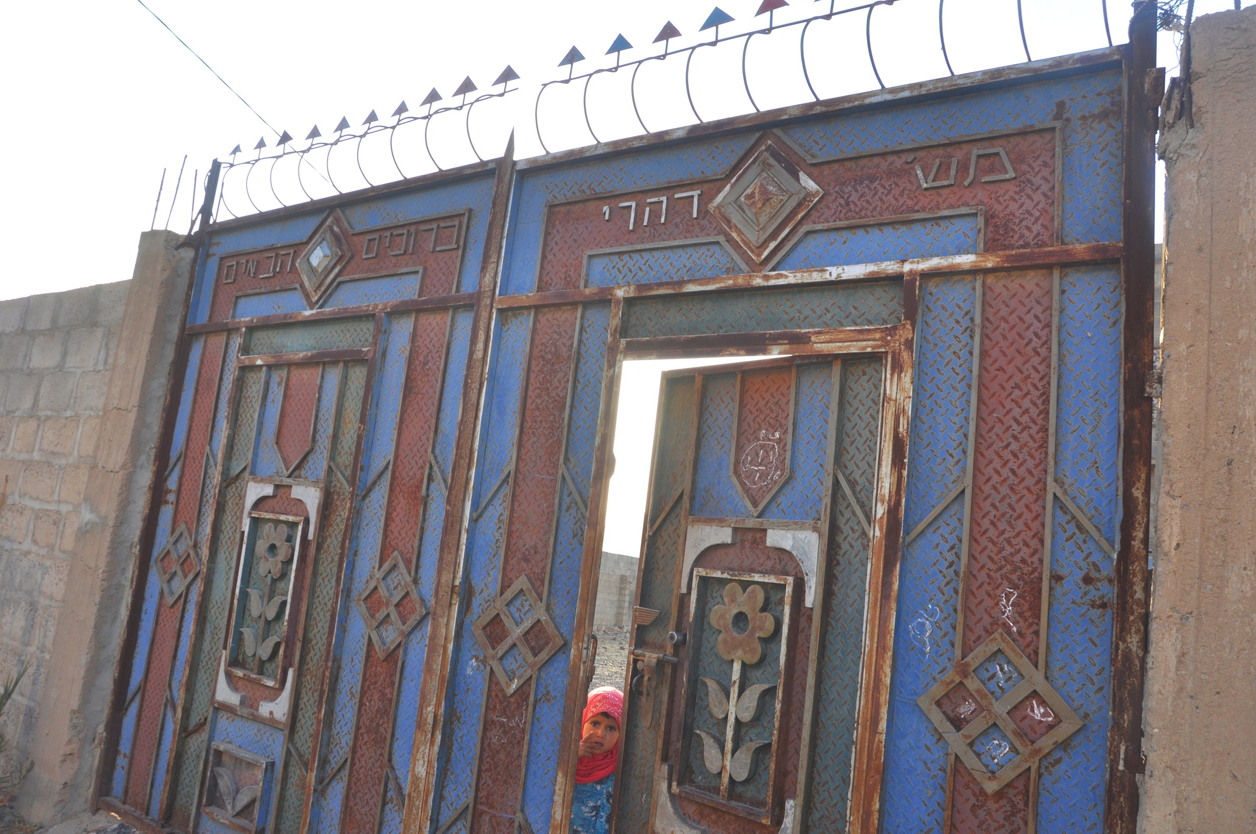 A child peeks through the gate of one of the historically-Jewish homes in Raydah. Photographed by the author.
