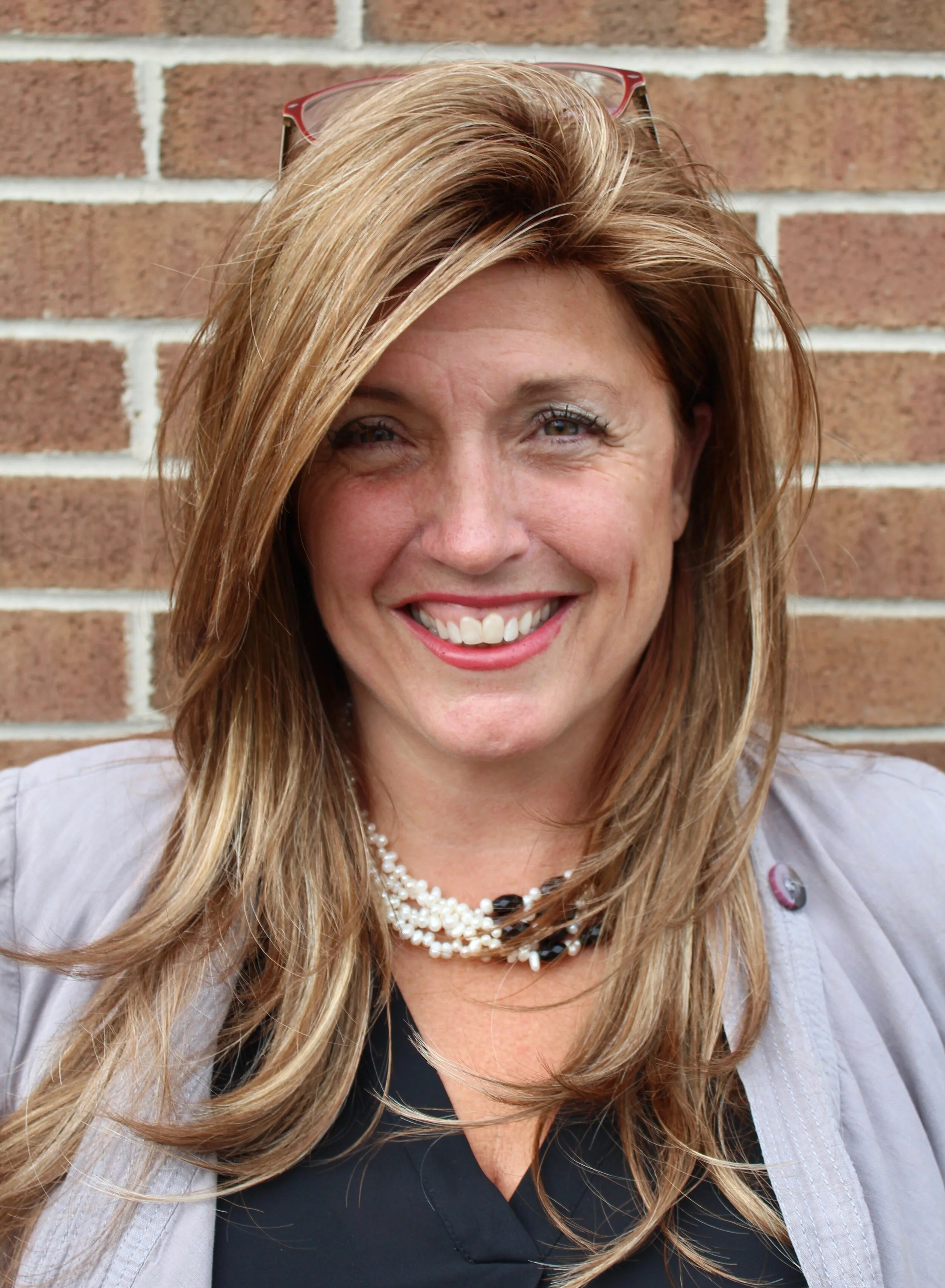 A woman in front of a brick wall smiling.