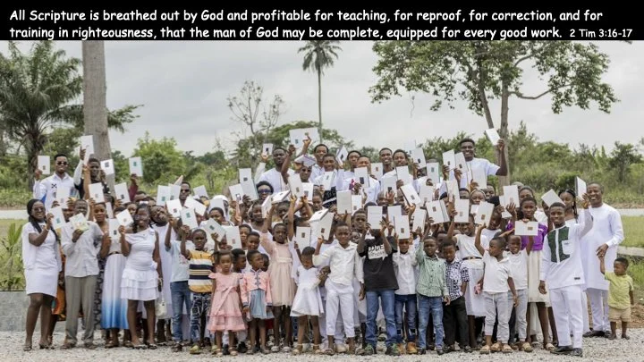 Group of men, women, and children outdoors holding Bibles, with some raising their hands, under trees and cloudy sky, celebrating or participating in a religious gathering.