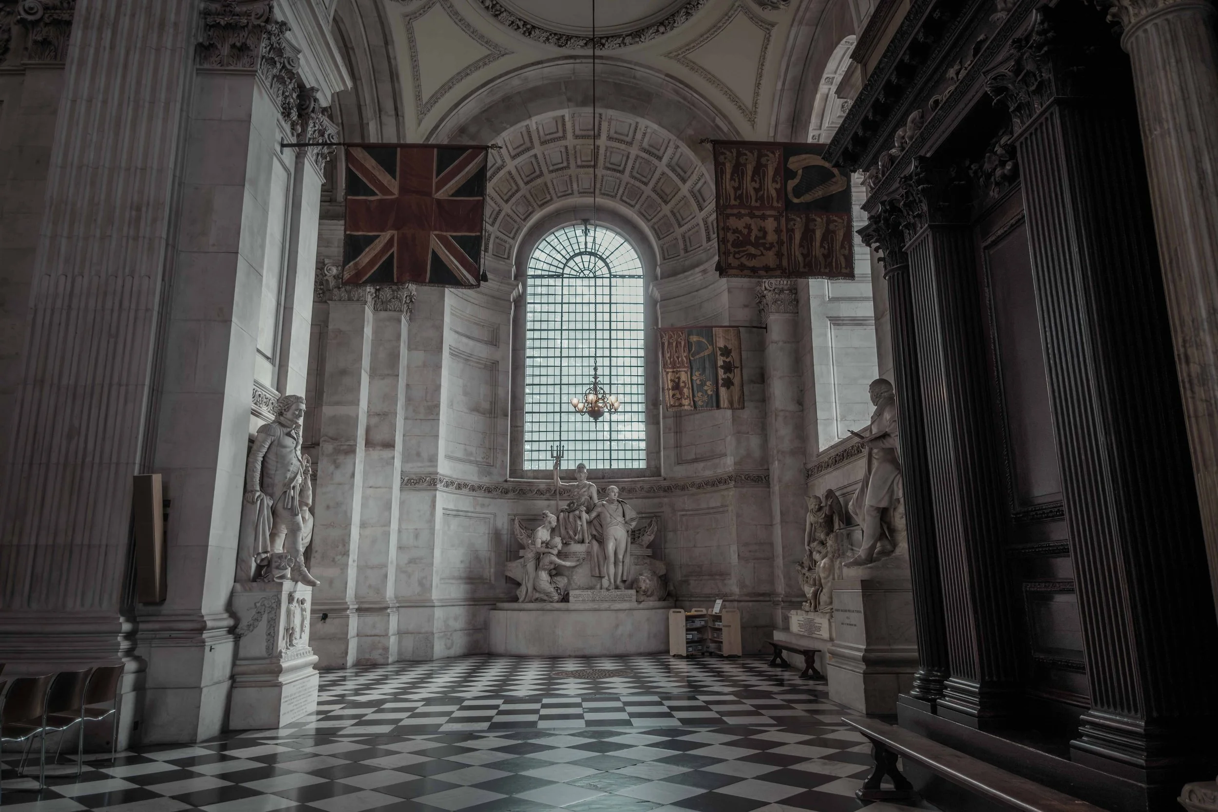 Memorial sculptures and historic flags inside St Paul's Cathedral, with a black-and-white chequered marble floor.