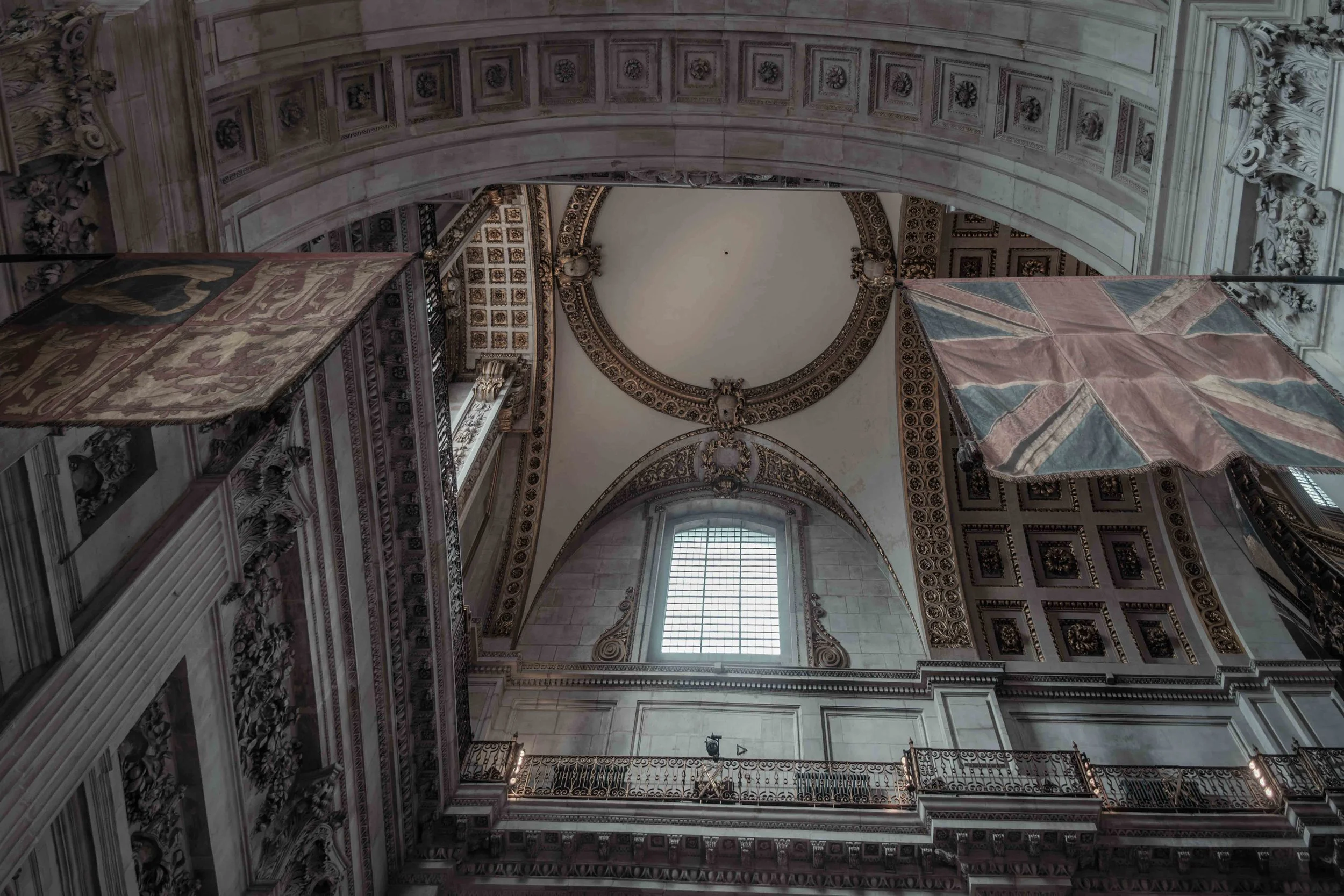 Looking upwards at the vaulted architecture of St Paul's Cathedral, with historic flags hanging beneath the arches.