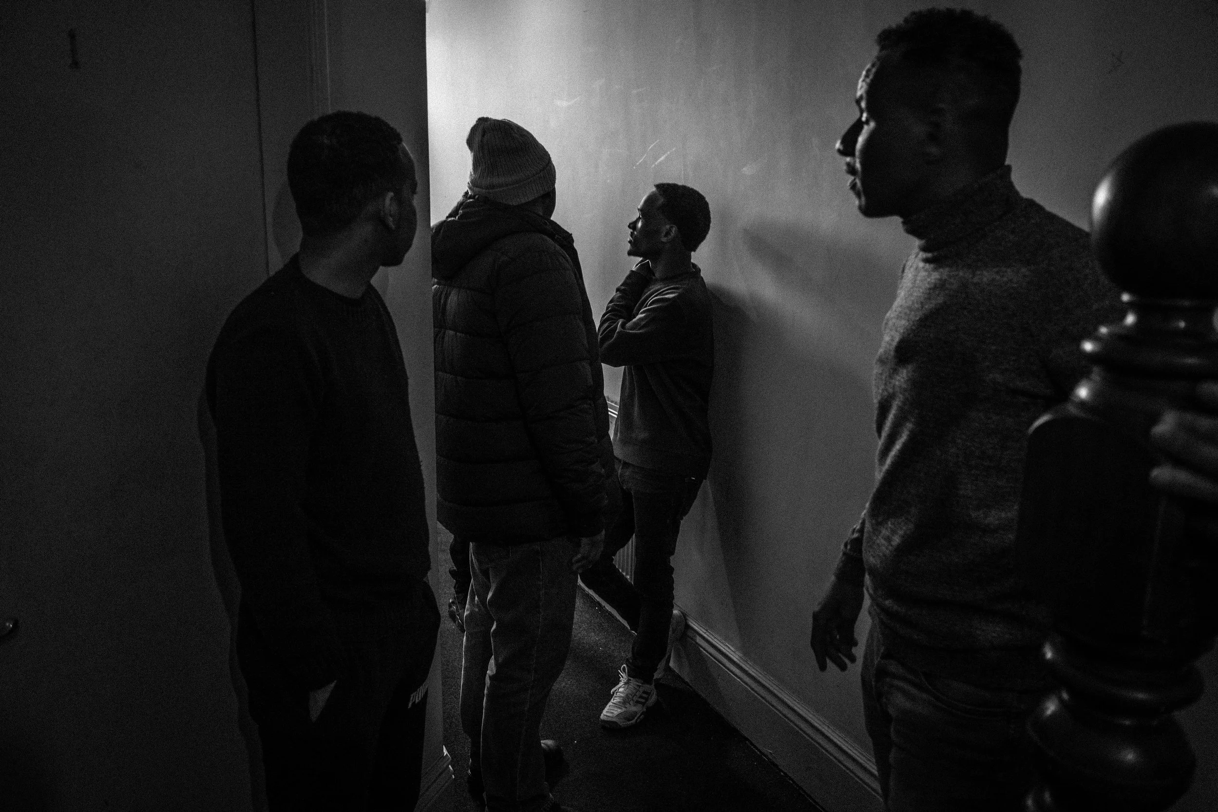 A group of young men standing in a dimly lit hallway, engaged in conversation.