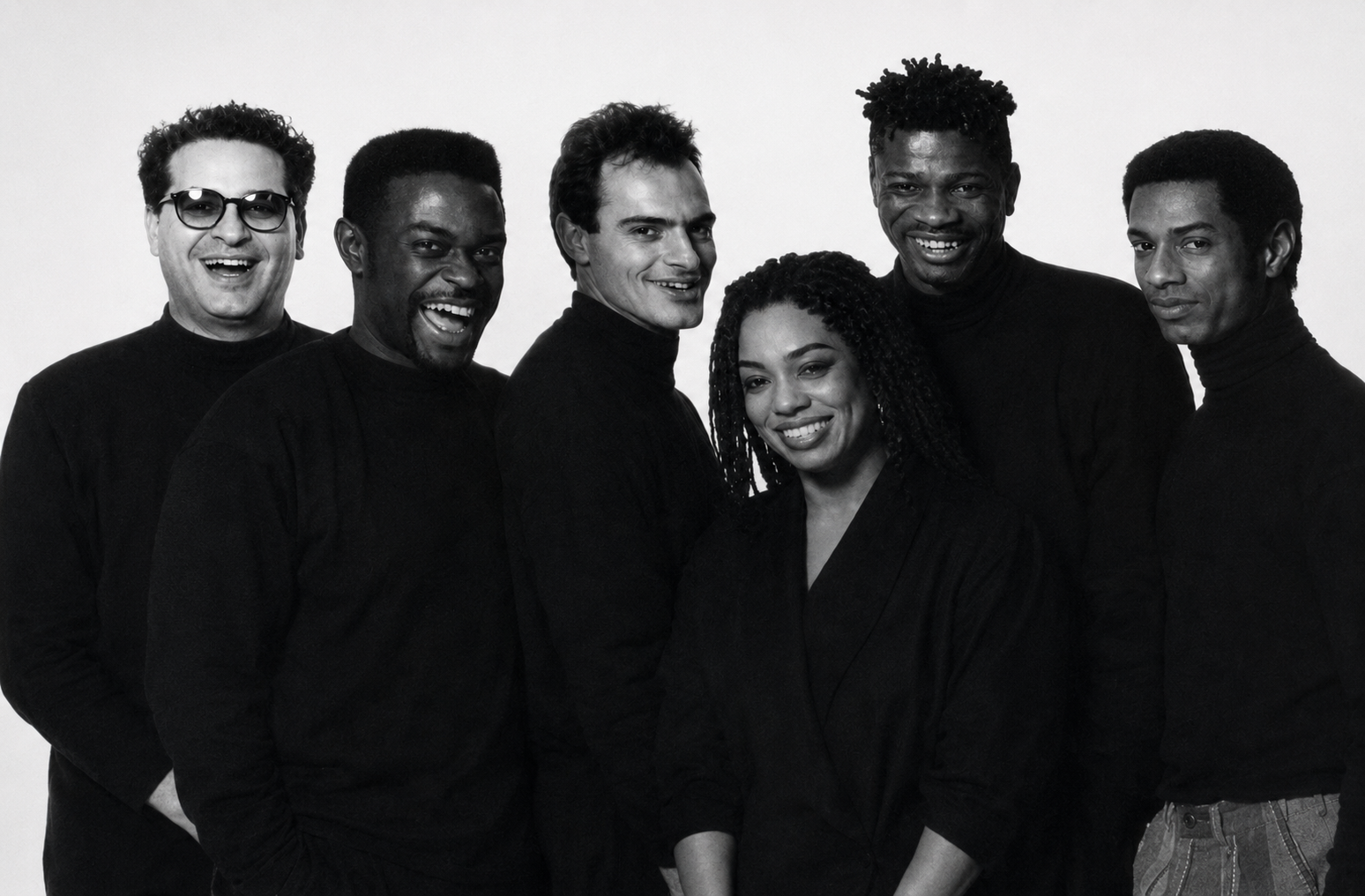A group of six diverse people standing together against a plain background, smiling and facing the camera.
