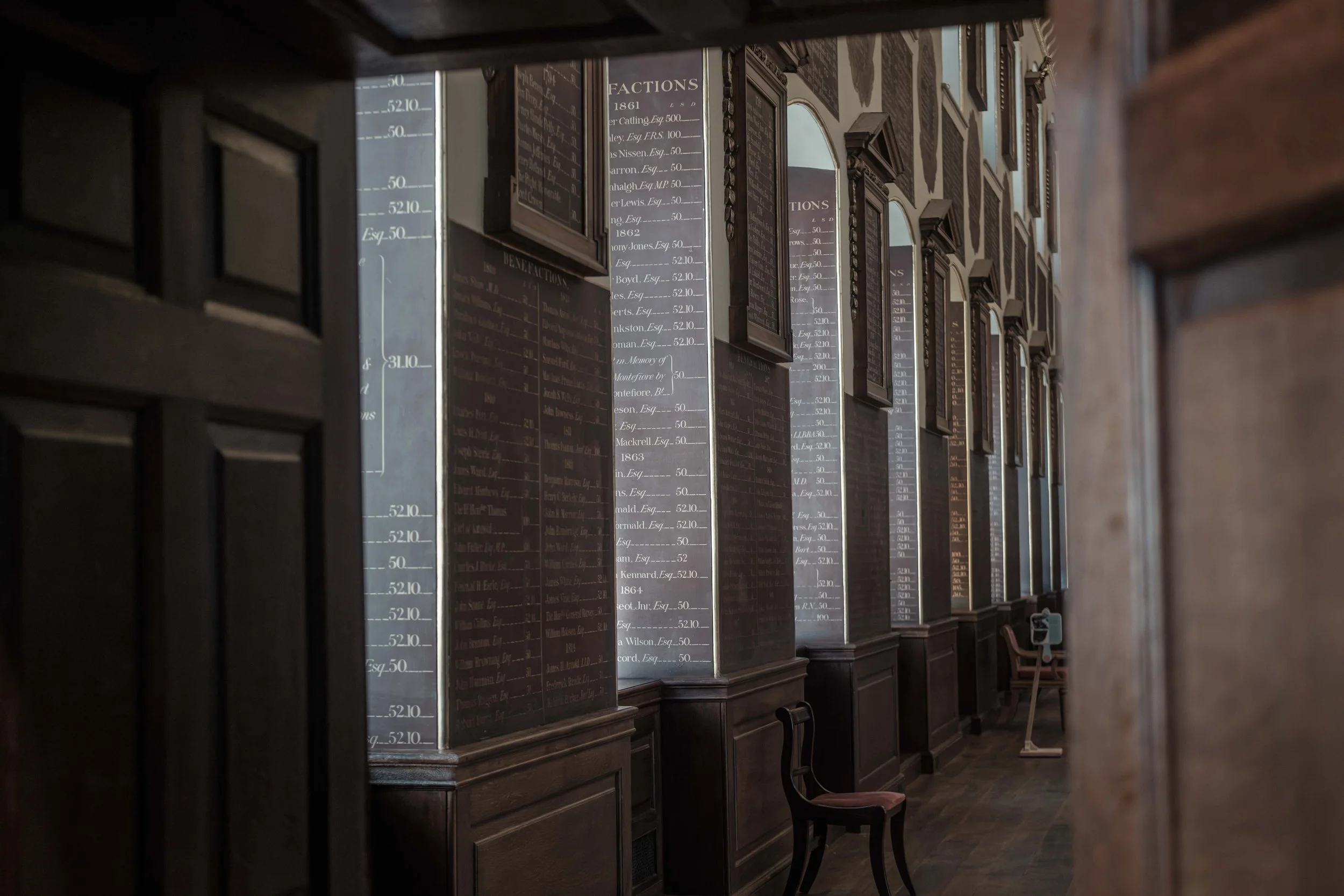 Historic wooden benefactors' boards lining a corridor at St Bartholomew's Hospital, recording names and donations.