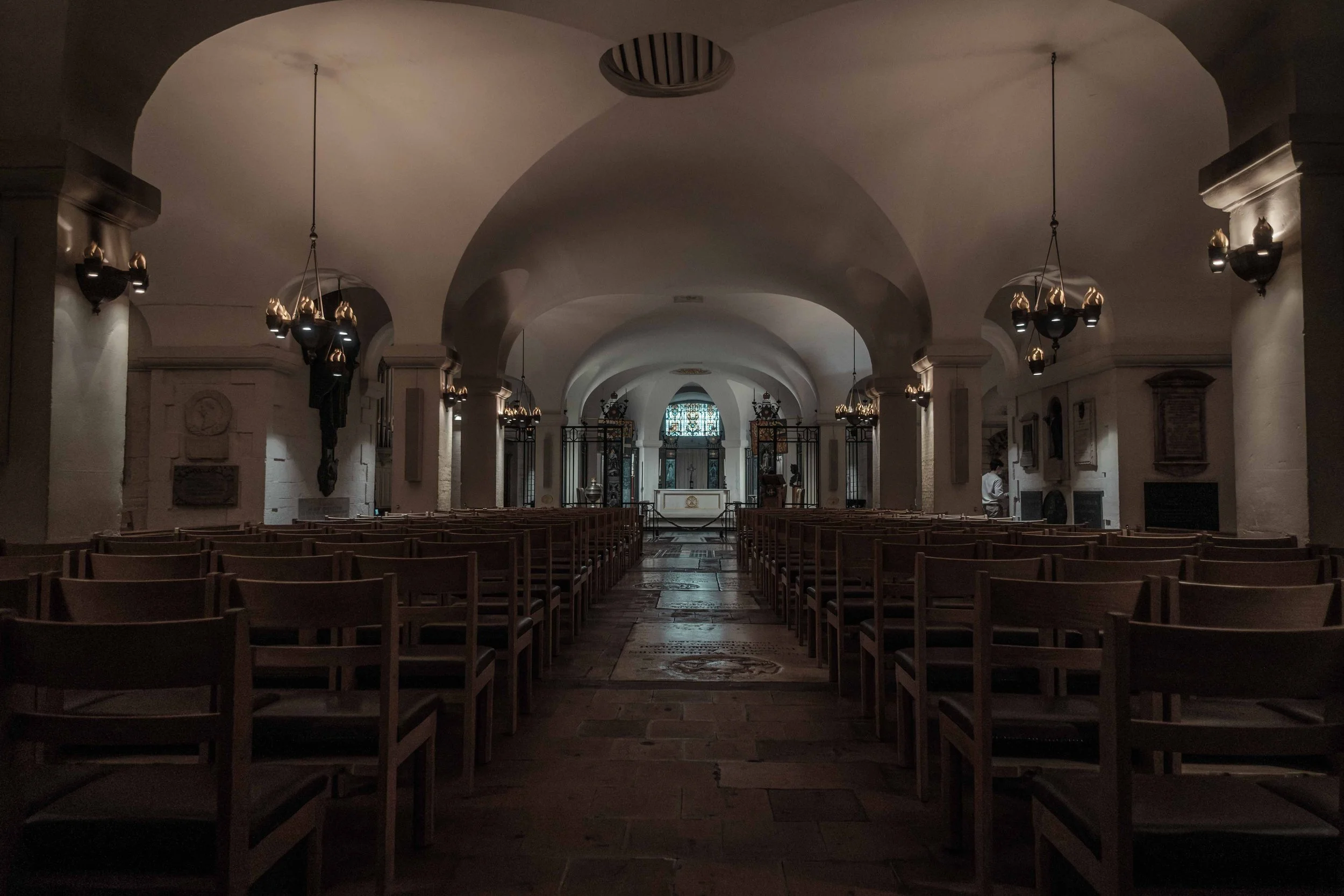 Quiet chapel in the crypt of St Paul's Cathedral, with rows of wooden chairs leading towards a small altar.
