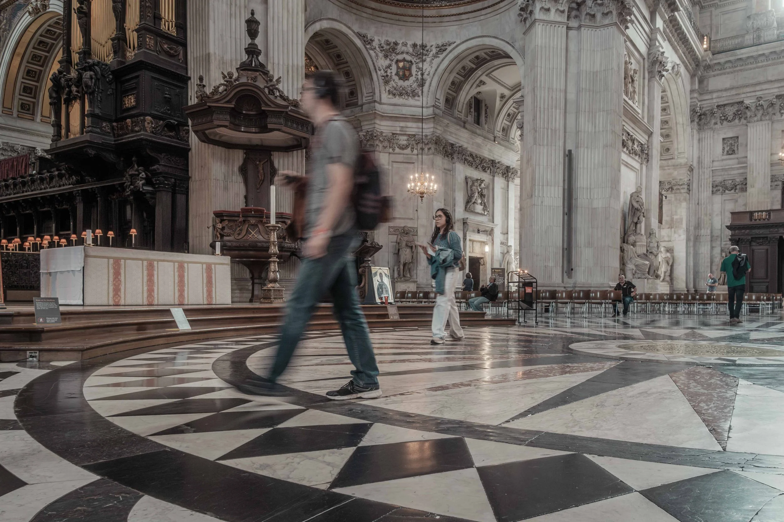 Visitors walking through the ornate interior of St Paul's Cathedral, with its marble columns and patterned floor.