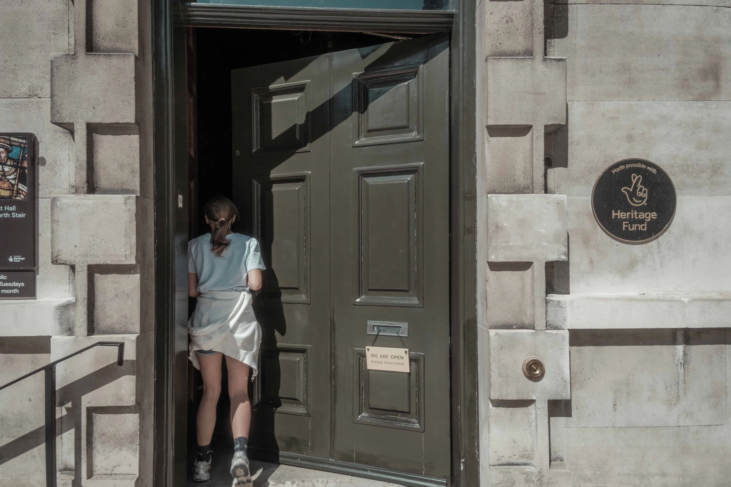 Visitor entering the historic Great Hall at St Bartholomew's Hospital through a large dark wooden doorway.