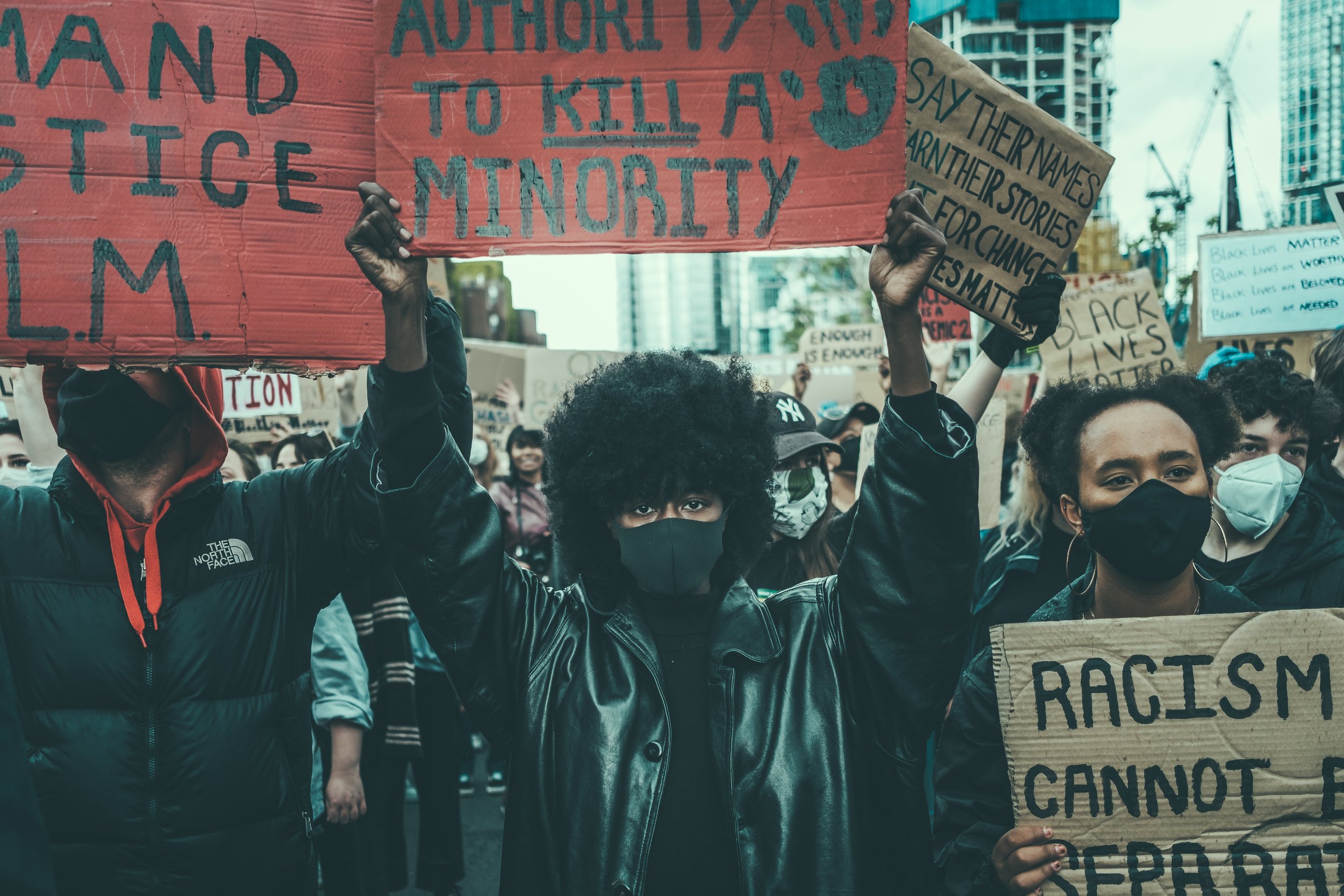 Group of diverse protestors holding signs at a street rally, with buildings and construction cranes in the background.