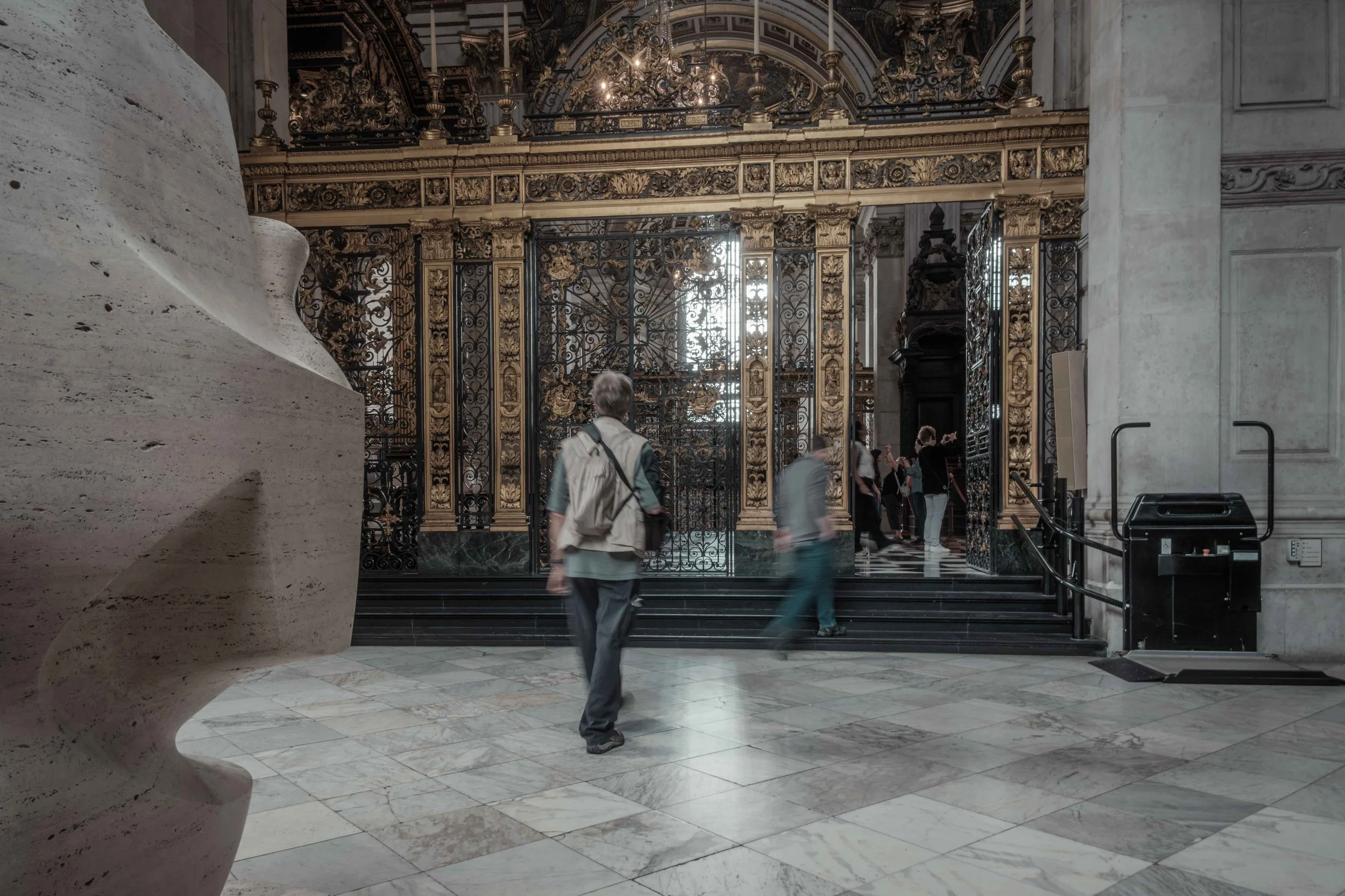Visitors walking past ornate gilded gates inside St Paul's Cathedral, London.