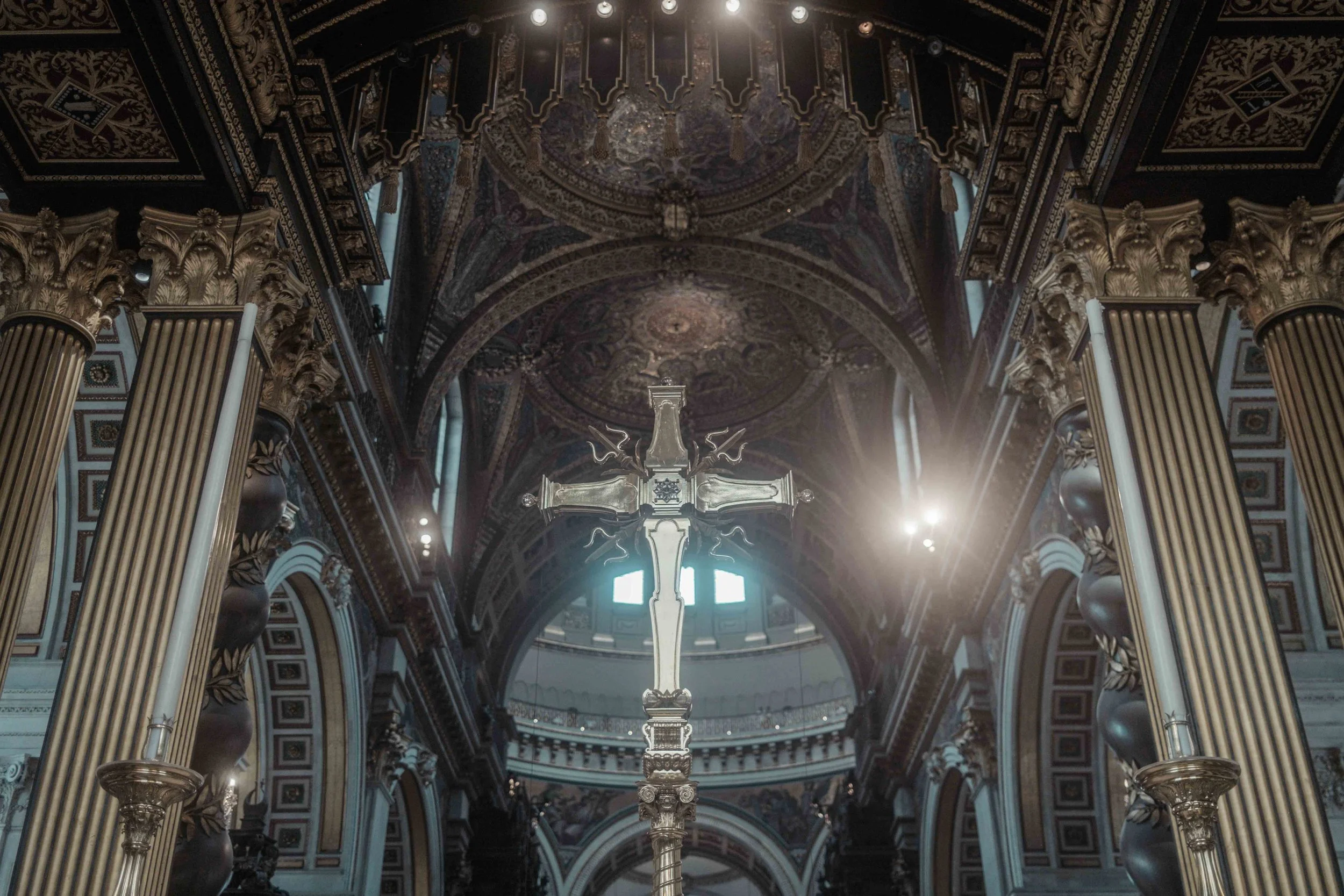 Ornate gold cross at the altar of St Paul's Cathedral, London, framed by decorated columns and vaulted ceilings.