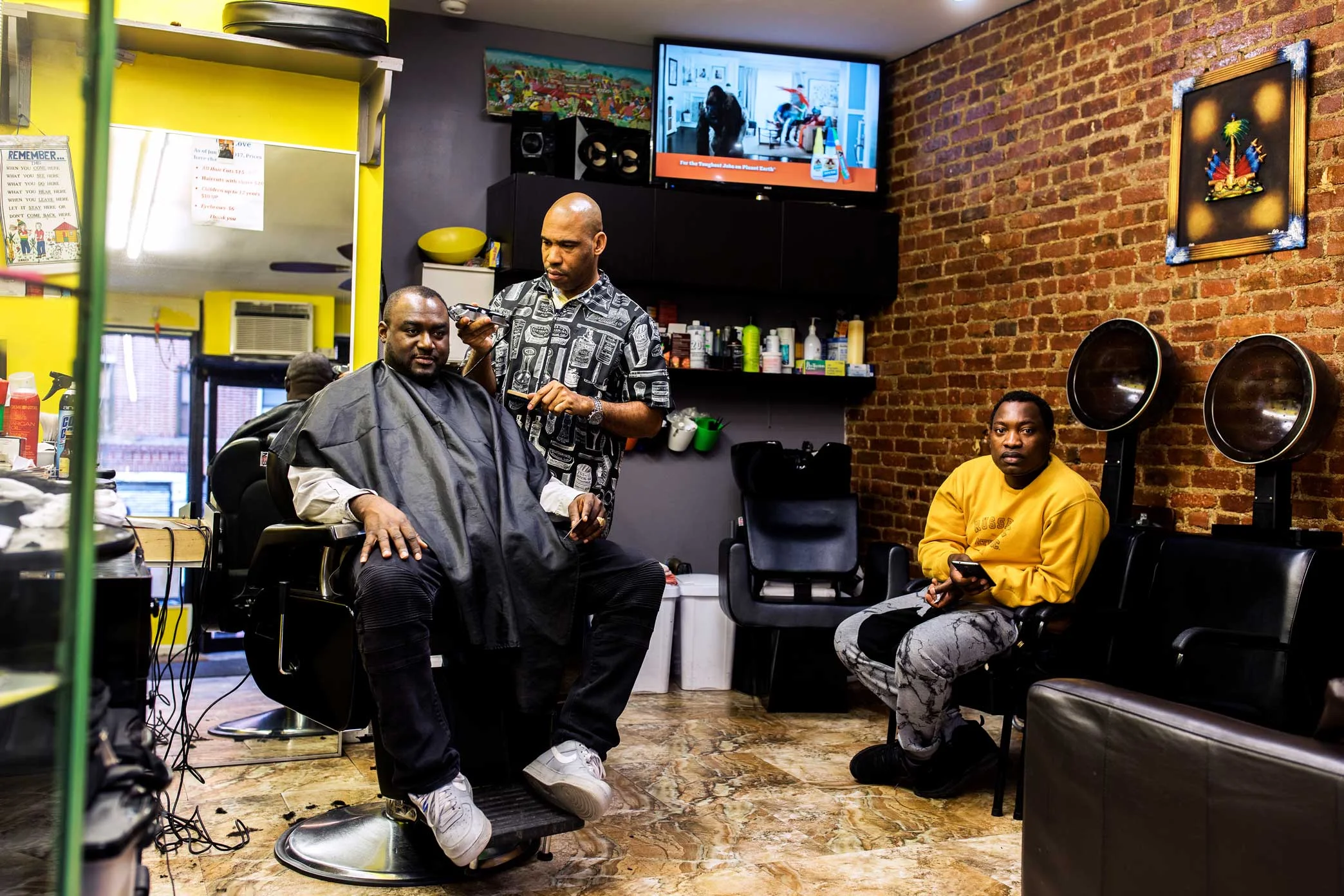 Ben Flambert, 42, left, at a Haitian-owned barbershop in Brooklyn, supports the idea of a Little Haiti district. “The Haitian presence out here is real strong,” he said. “It makes sense.”