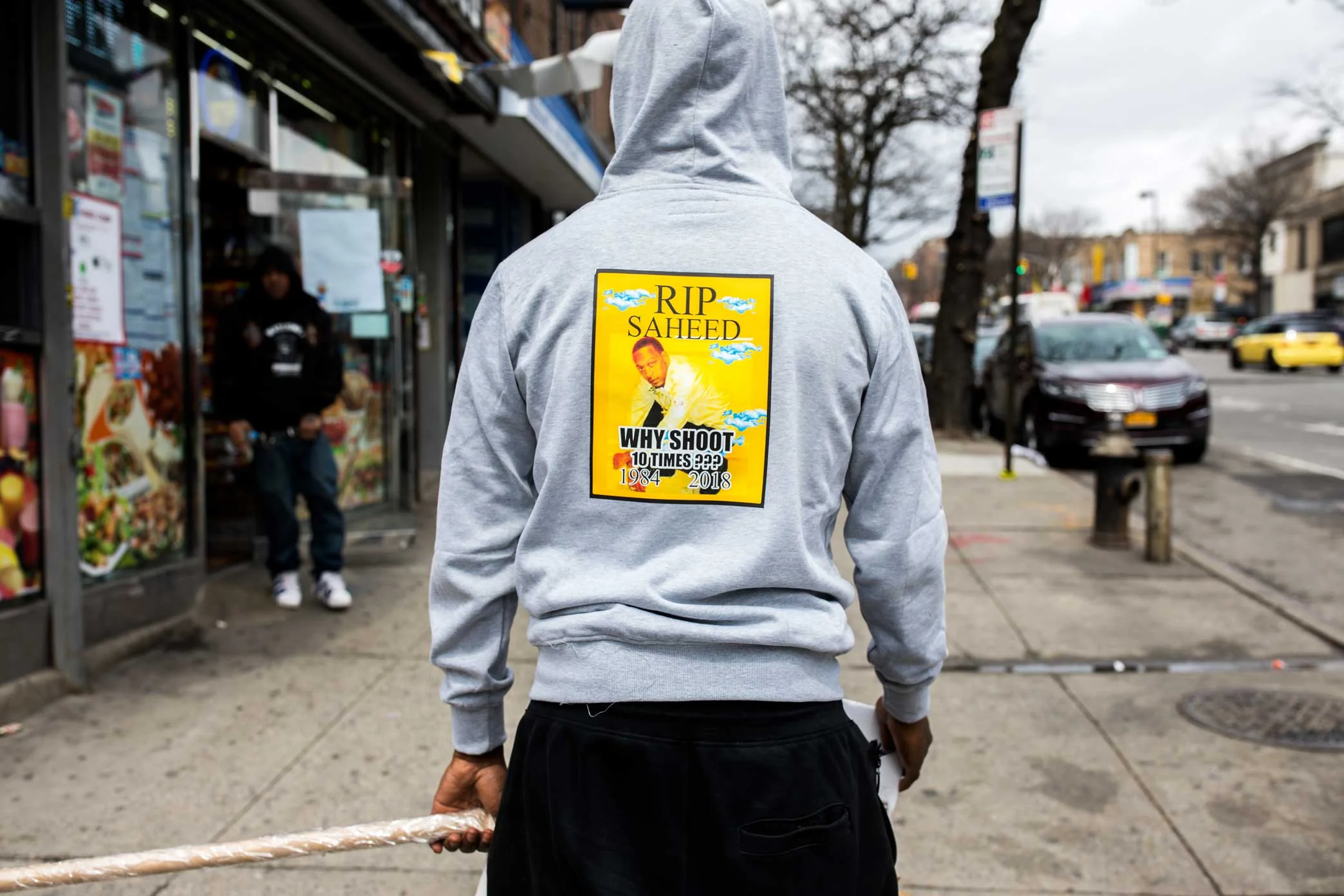 A man wearing a ‘R.I.P. Saheed’ shirt walking up Utica Ave carrying a 'Why Shoot' sign near the memorial site for Saheed Vassell in Crown Heights Brooklyn.