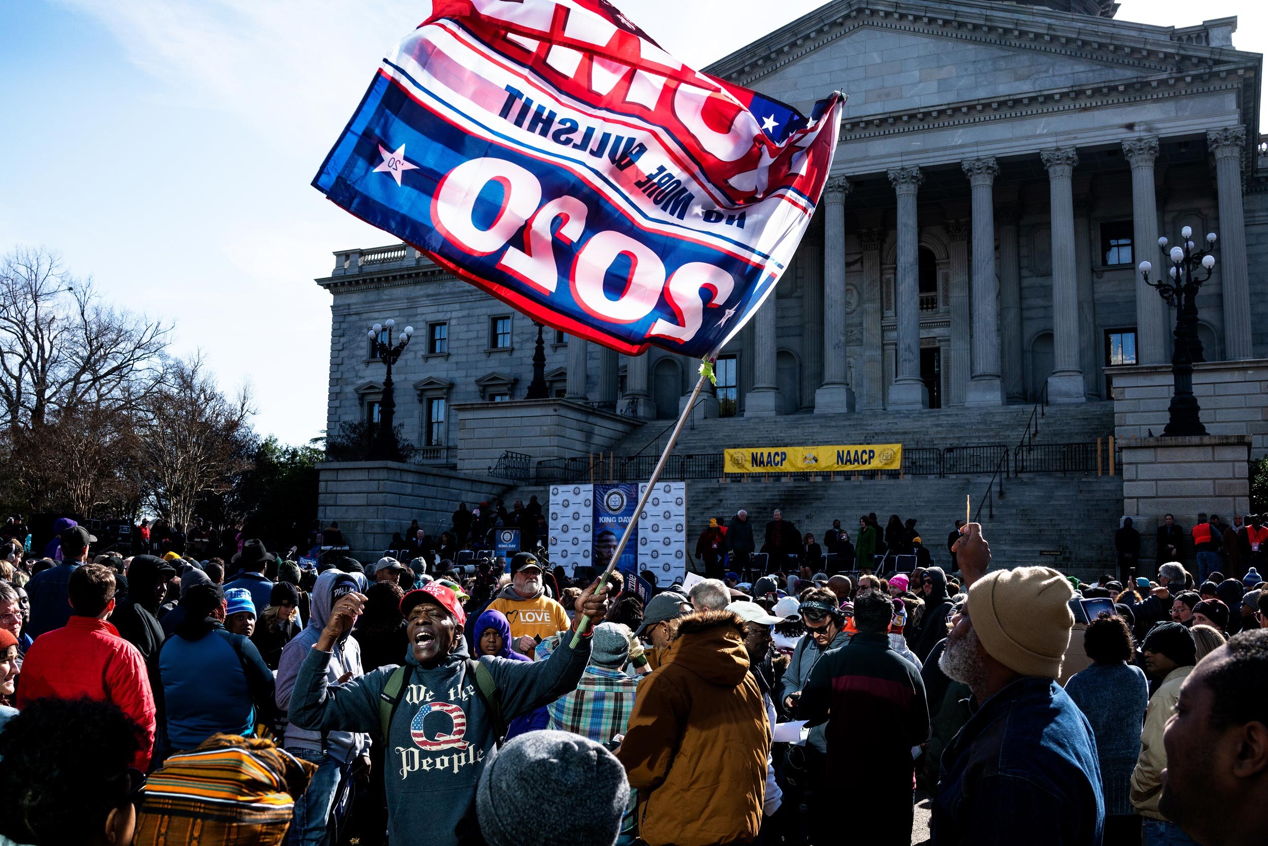   A Trump supporter shouts and waves a Trump 2020 flag during the MLK Day celebration at the South Carolina Statehouse in Columbia, South Carolina. In attendance was the 2020 Democratic candidates and state and city officials.   