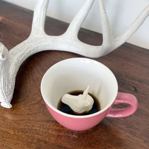 White unicorn revealed inside pink Creature Cup on minimalist countertop.