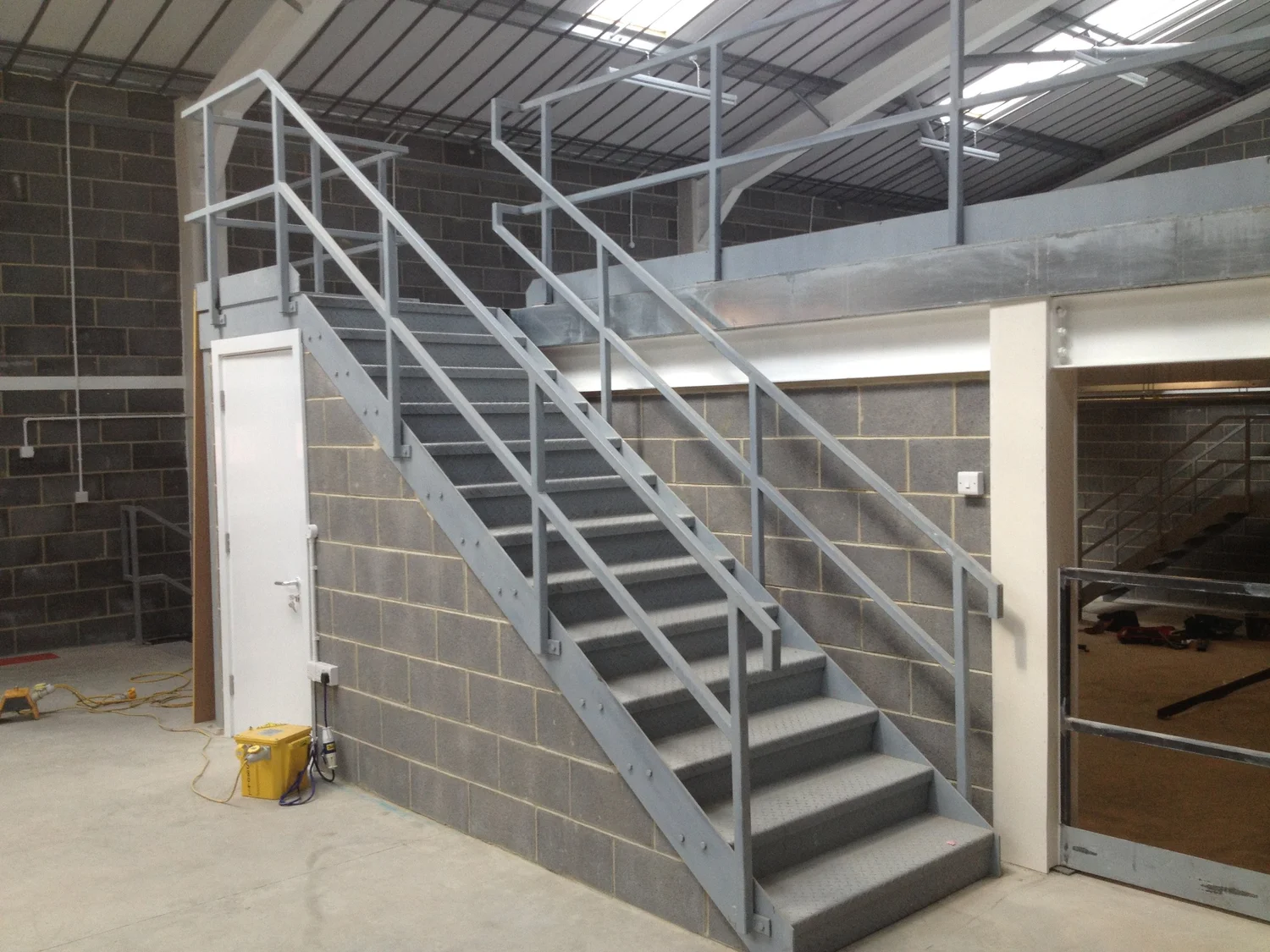 A galvanised SAFE-T-FAB industrial stair with handrails providing access to a warehouse mezzanine.