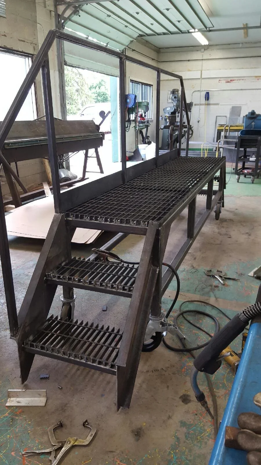A welded steel crossover with bar-grating treads and stair stringers, standing complete on the fabrication floor before finishing.