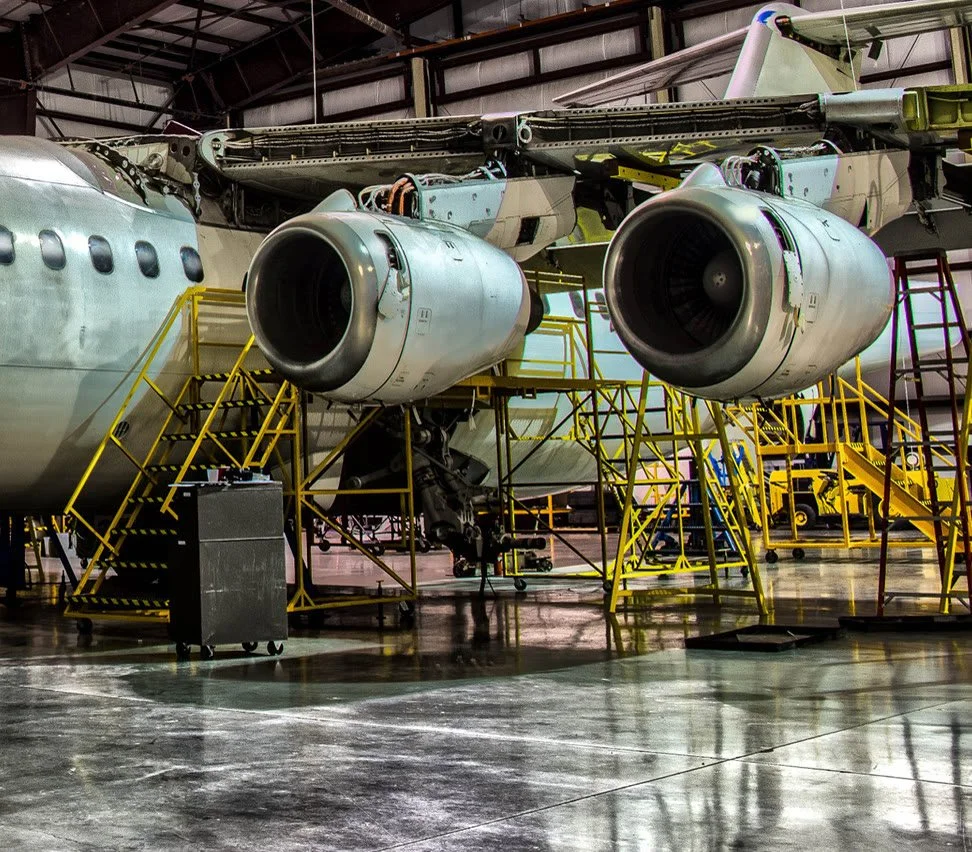 Yellow SAFE-T-FAB maintenance stands beneath the engines and wing of a fixed-wing aircraft in a hangar.