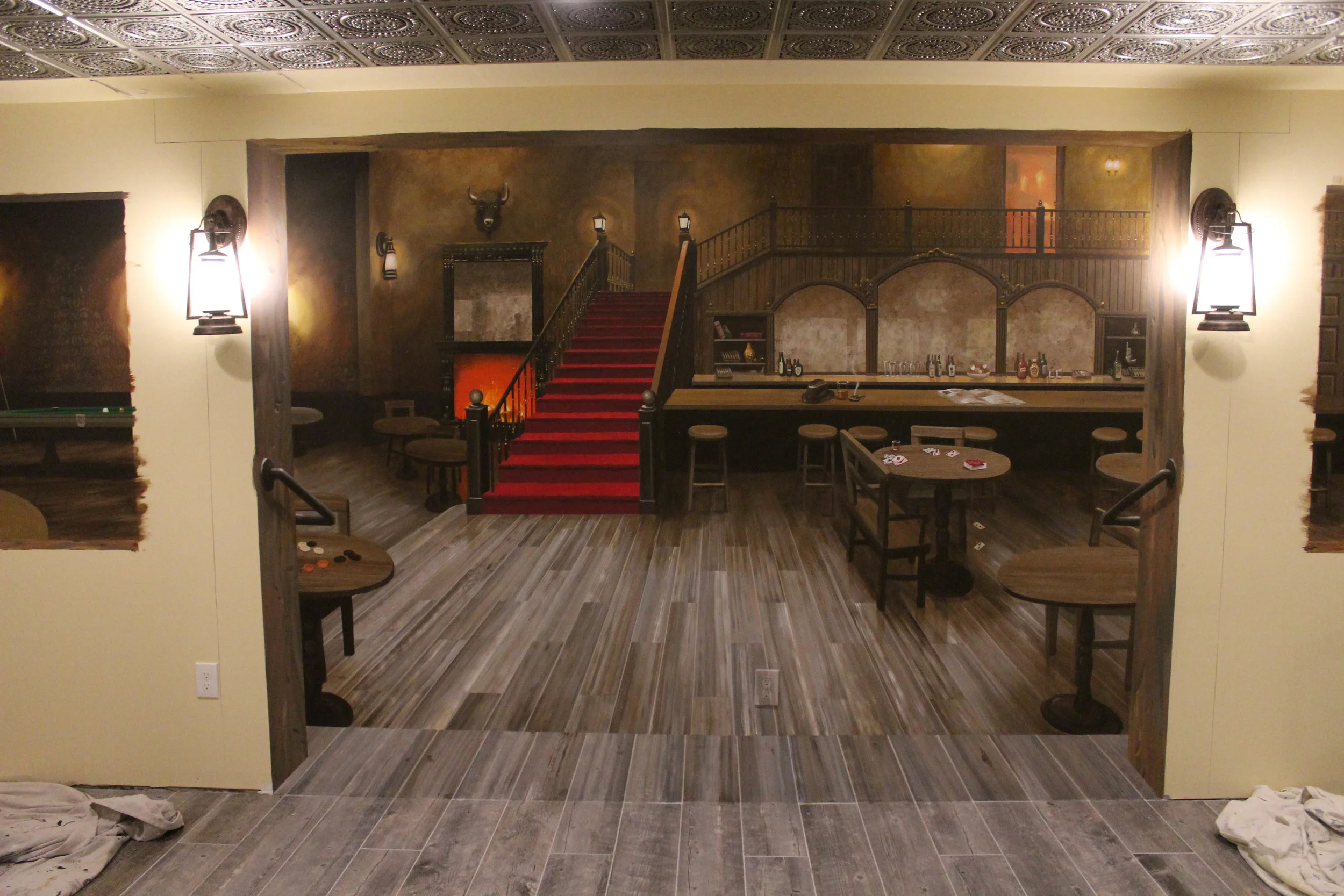 This photo shows the trompe l'oeil mural prior to the installation of surrounding trim. The floor of the room is matched into the mural to create the sense that the room continues. The scene within the mural depicts an old western hotel lobby and bar. The details within the mural will be echoed in reality by the details within the actual bar room.