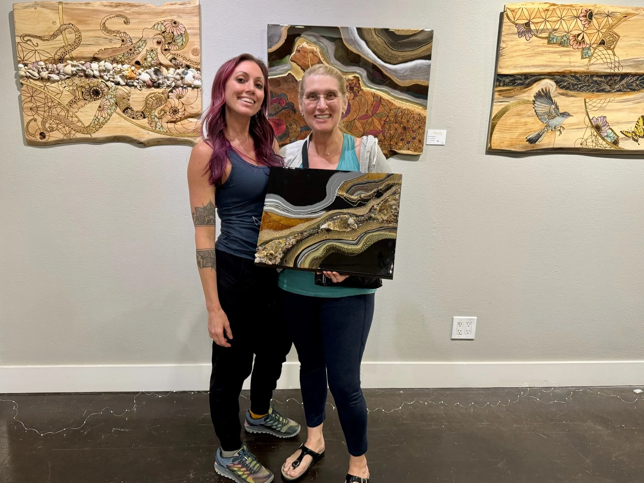  Anne Shackelford at the Artful Connections gallery exhibit at Artworks Gallery, pictured with the patron who won the art raffle. Surrounded by her wood burned and resin mixed media pieces, this moment celebrates the connection between artist, collec