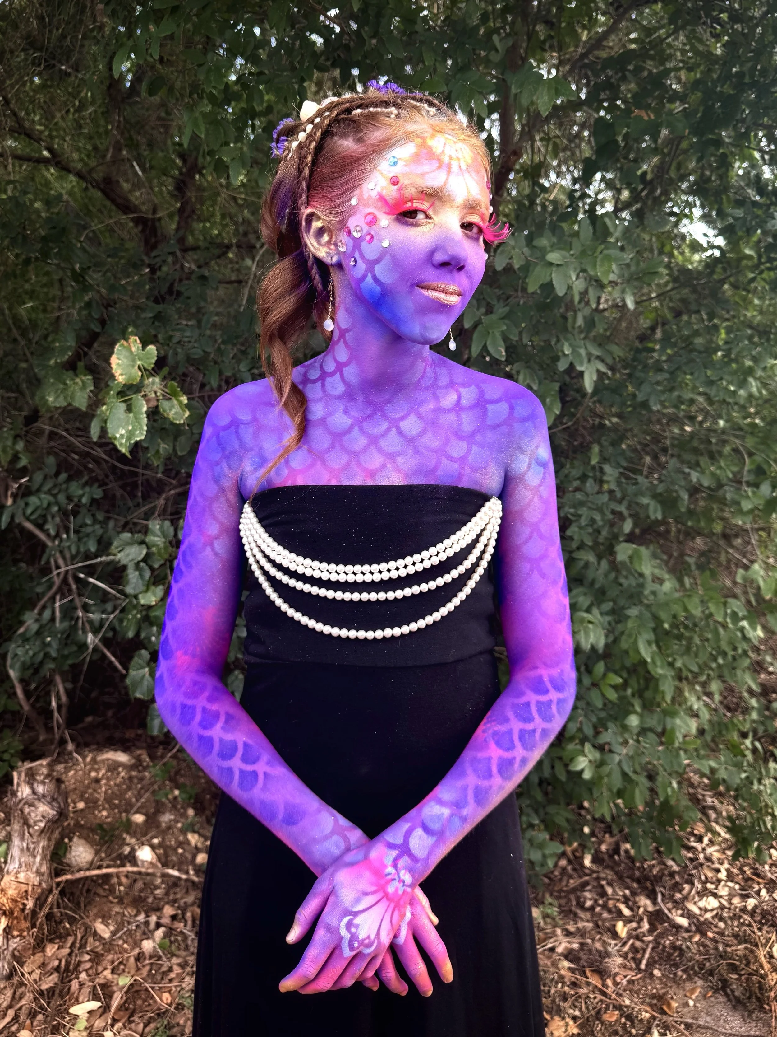   Mermaid-inspired body art  created by Austin artist Anne Shackelford for Violet, layered in purples, pinks, blues, and gold. Embellished with gems, pearls, and seashells, photographed at sunset to capture her luminous glow. 2025. 