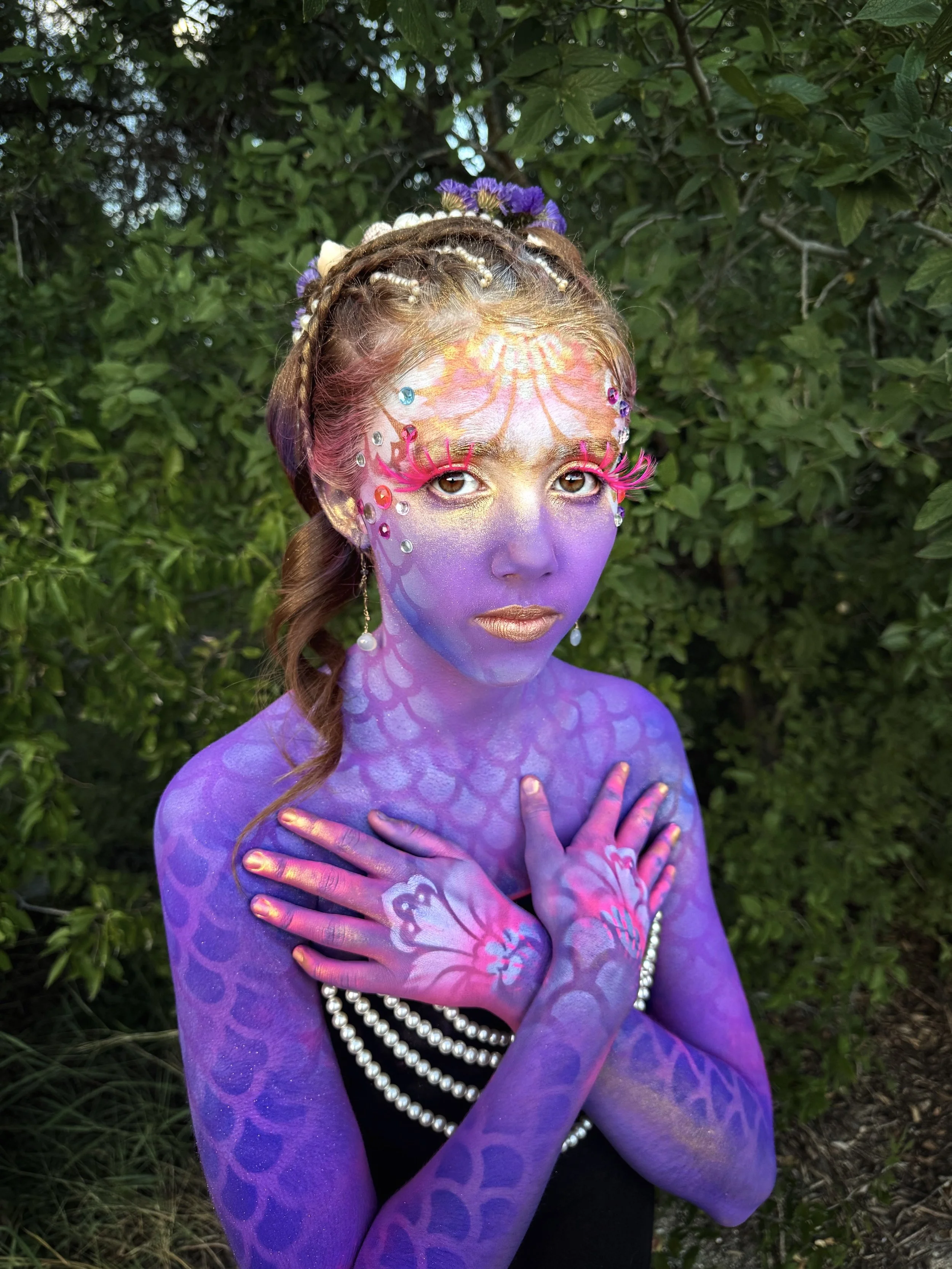  Thirteen-year-old Violet transformed into a glowing mermaid with body paint by  Anne Shackelford . Featuring hand-painted scales, shimmer pigment, jewels, pearls, and seashell accents for a radiant, oceanic-inspired look. 2025. 