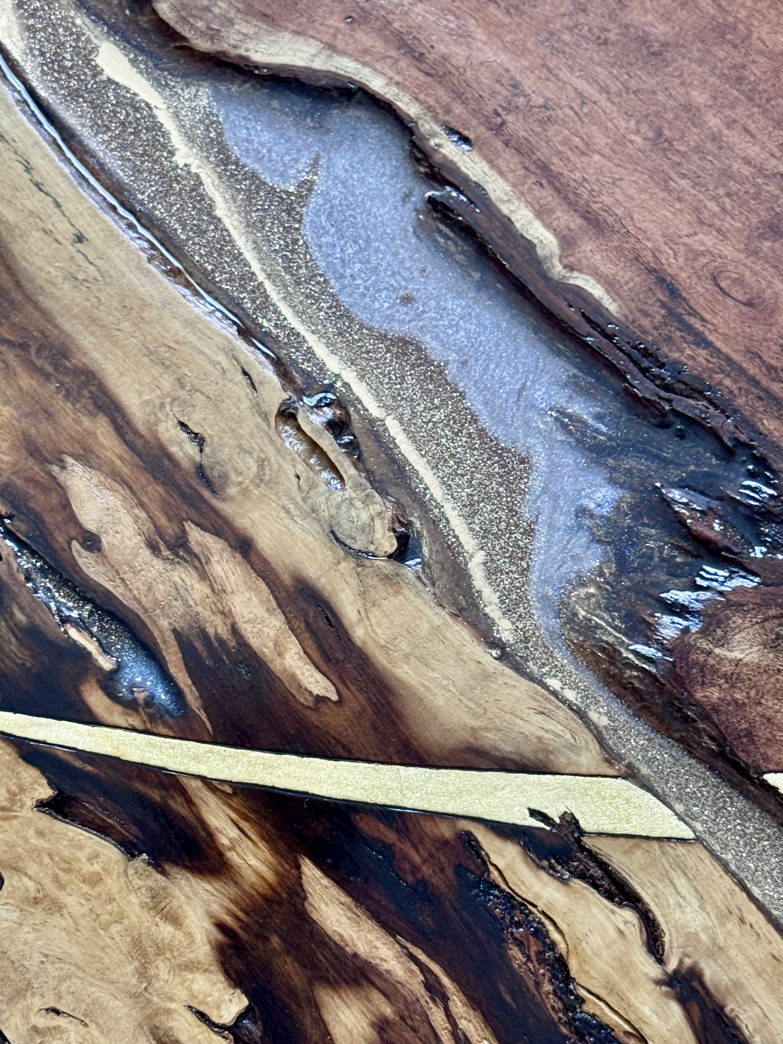 Close-up of opal resin flowing through the natural wood grain beside a geometric metal leaf detail.