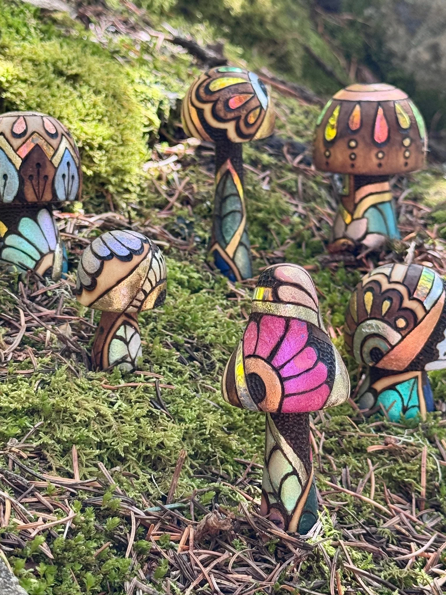 Handcrafted light-responsive wooden mushroom sculptures with shimmering metallic finishes and colorful botanical patterns, nestled among moss and woodland greenery.