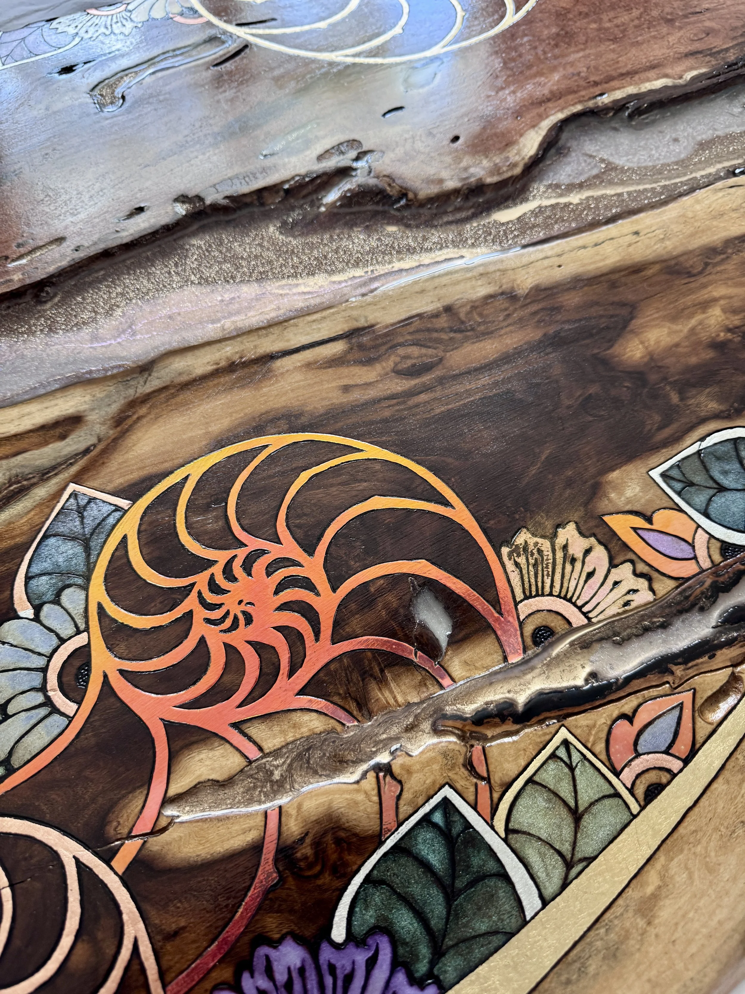 Close-up of pyrography and colorful botanical patterns flowing through the natural grain and live edge of Texas wood.