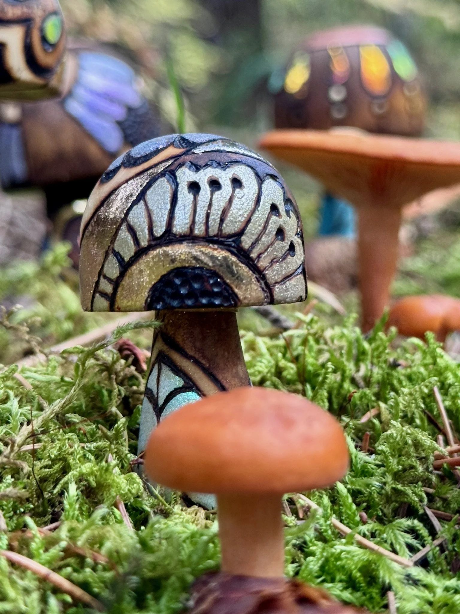 Close-up of a small handmade wooden mushroom with silver and gold detailing, dark pyrography outlines, and a turquoise patterned stem.